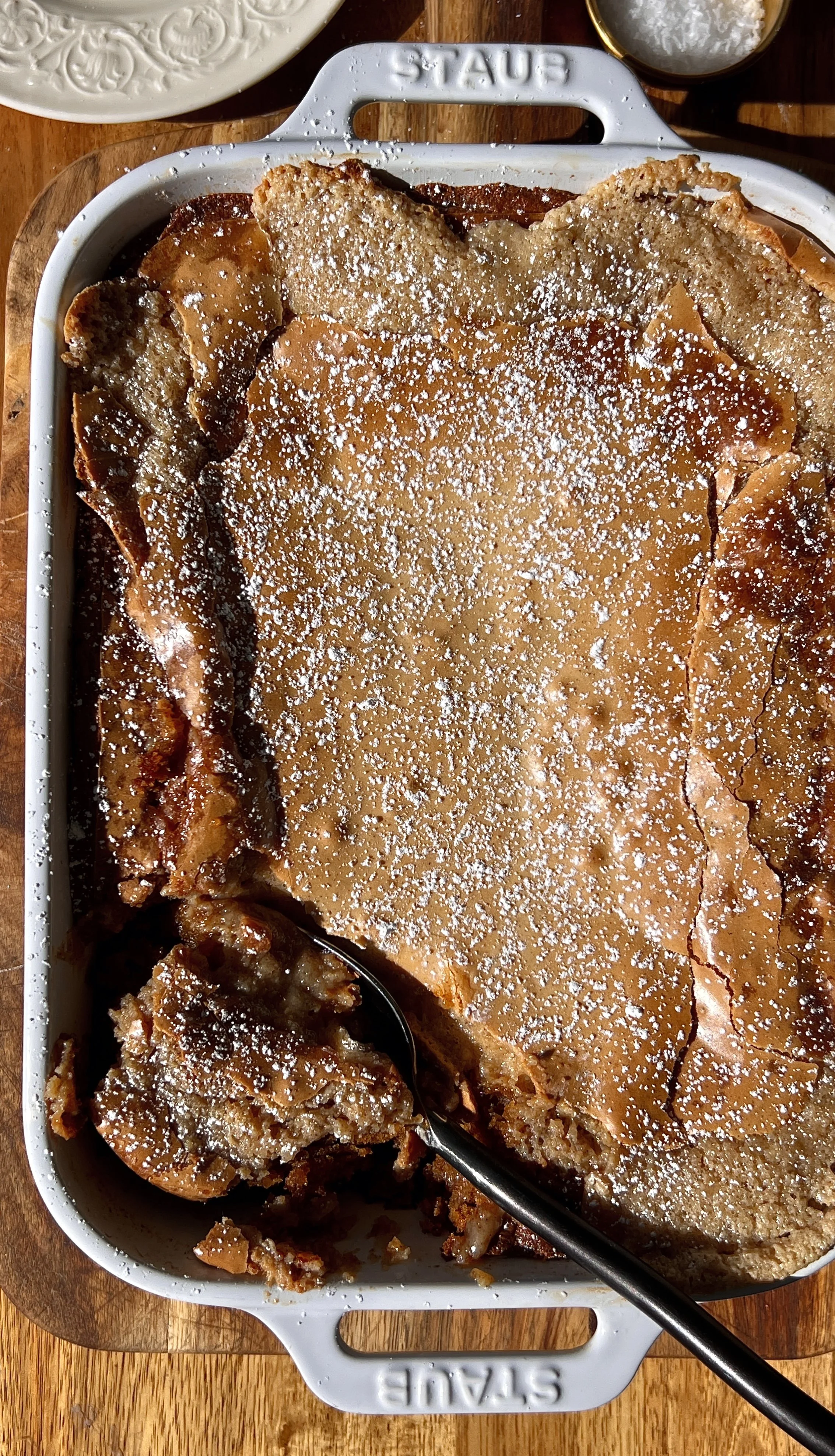 Deep dish sweet potato gooey brown butter cake with a spoon taken out showing the soft tender spiced brown butter sweet potato base and rich gooey cinnamon cream cheese layer melting together inside.