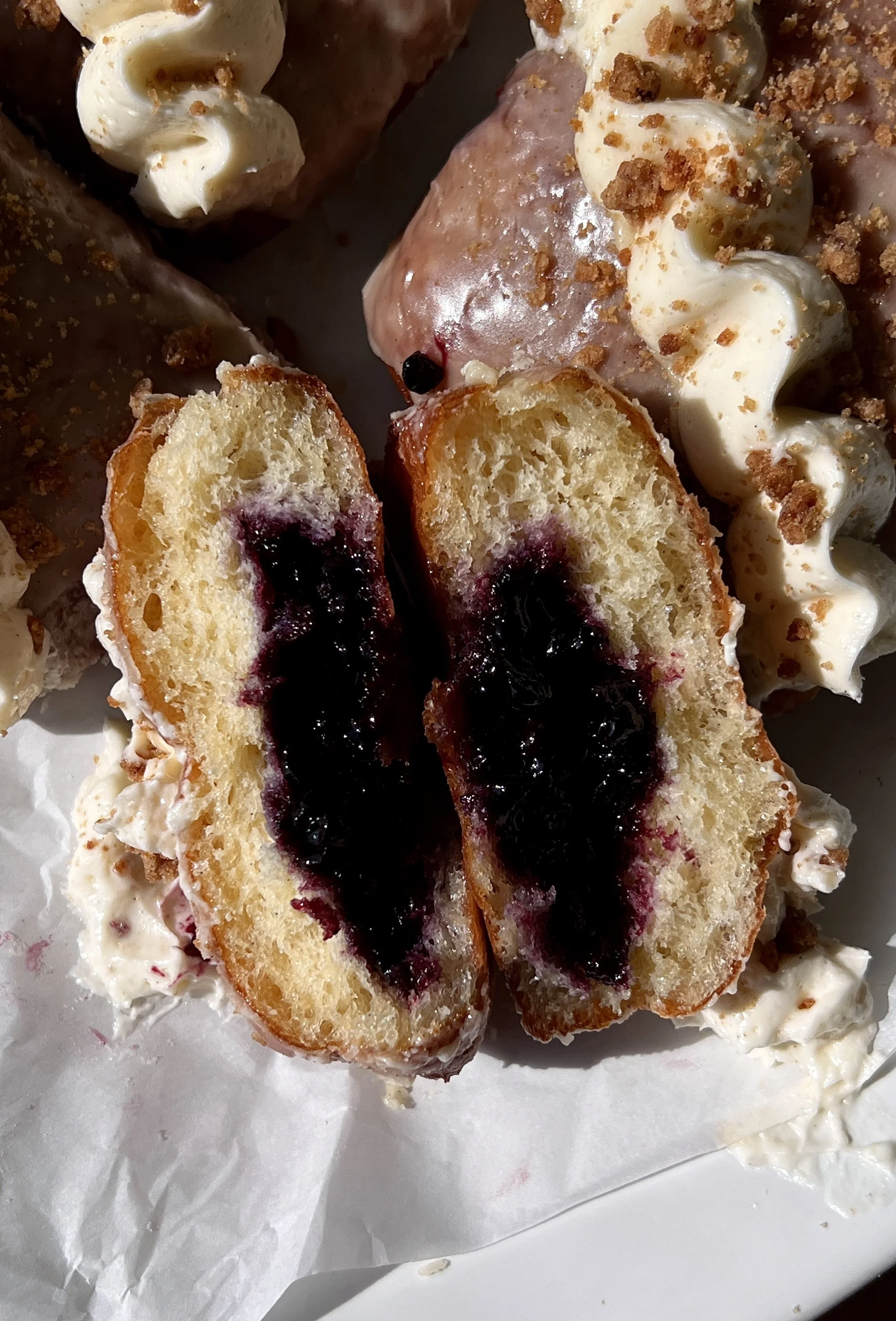 Blueberry pie donut bar with a bite taken out showing the homemade blueberry compote filling inside coated in a vanilla bean glaze with whipped buttercream and shortbread crumbles on top.