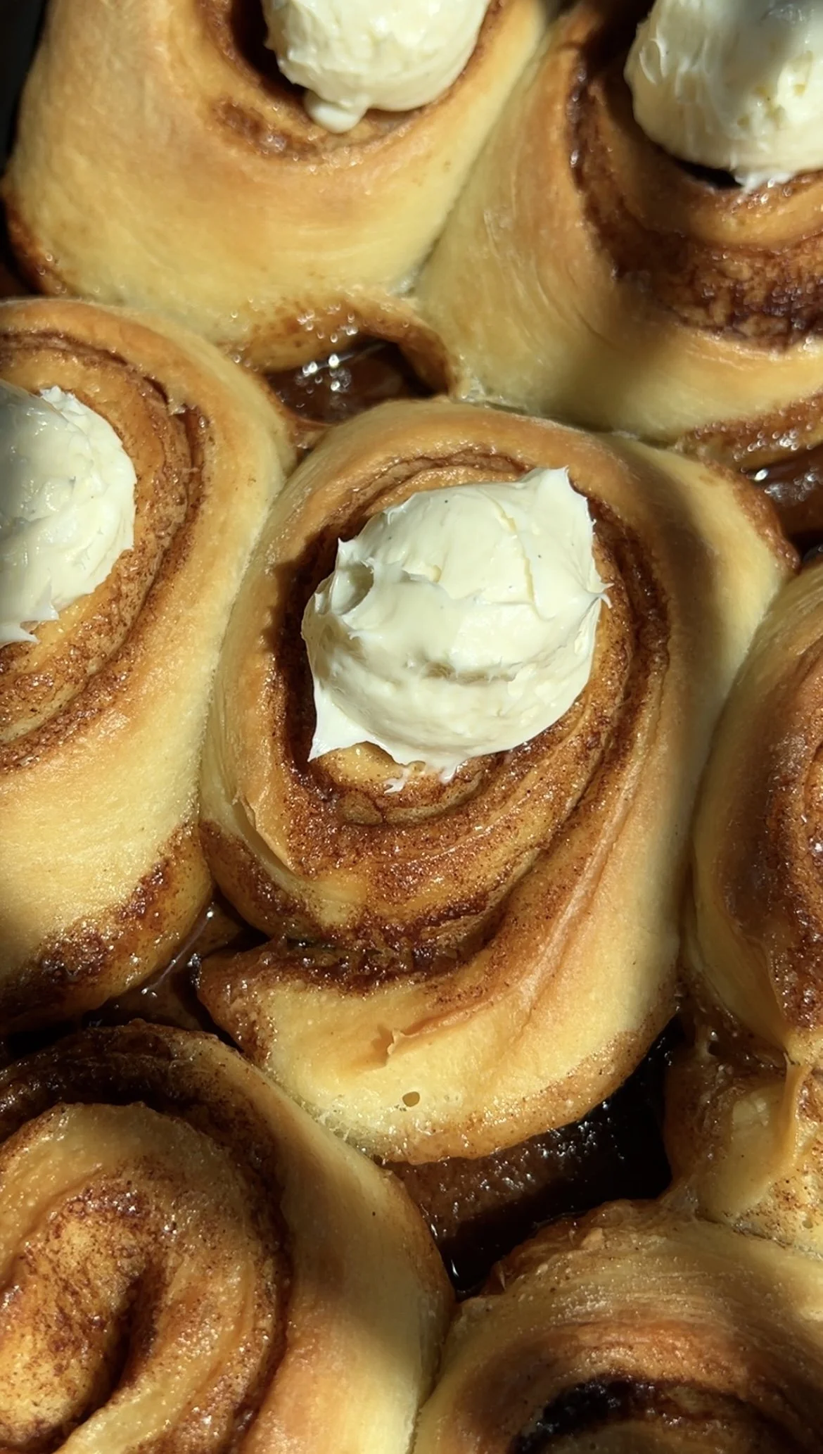 Close-up of Sourdough Cinnamon Rolls with a golden exterior, topped with cream cheese icing. The fluffy rolls are swirled with cinnamon sugar filling, promising a decadent treat. The icing adds a creamy finishing touch to these homemade delights.