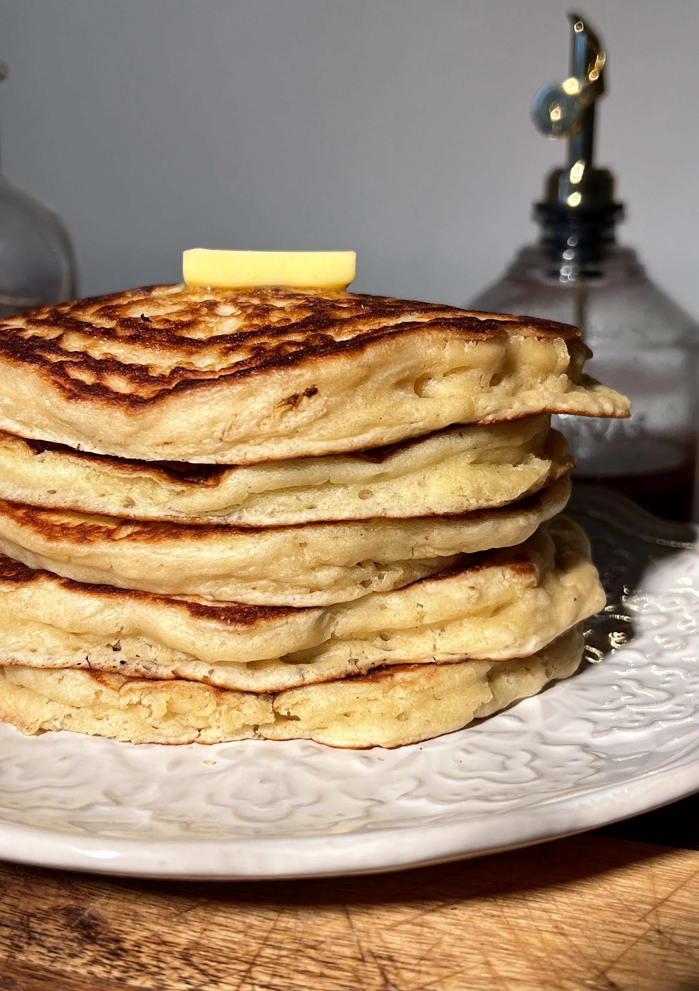Classic buttermilk pancakes stacked high on a plate, soft and fluffy with golden edges, topped with butter and maple syrup, served alongside a warm maple brown butter latte.