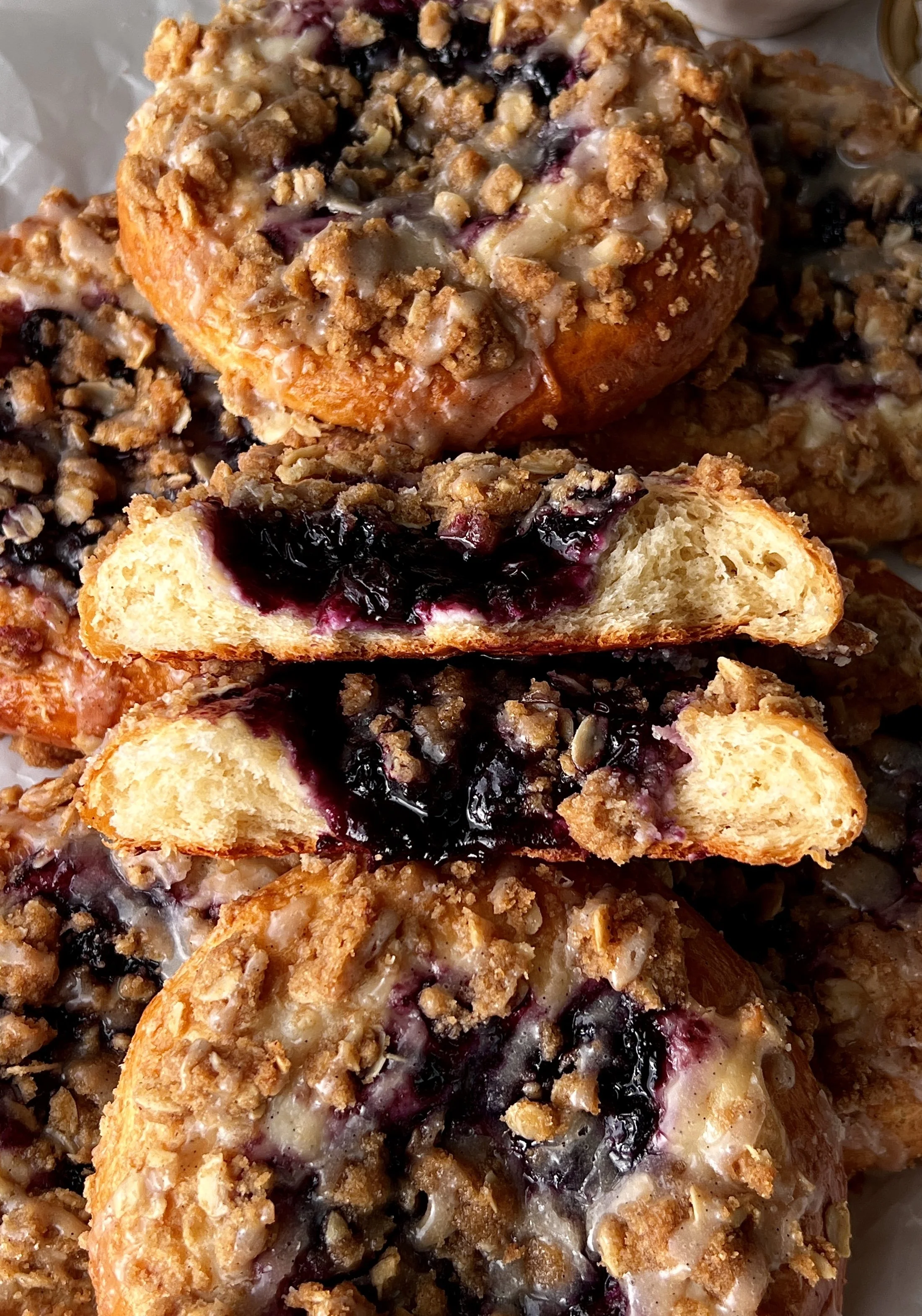 Blueberry cheesecake streusel bun being pulled apart showing the soft pillowy dough, rich cheesecake filling, and homemade jammy blueberry compote inside.