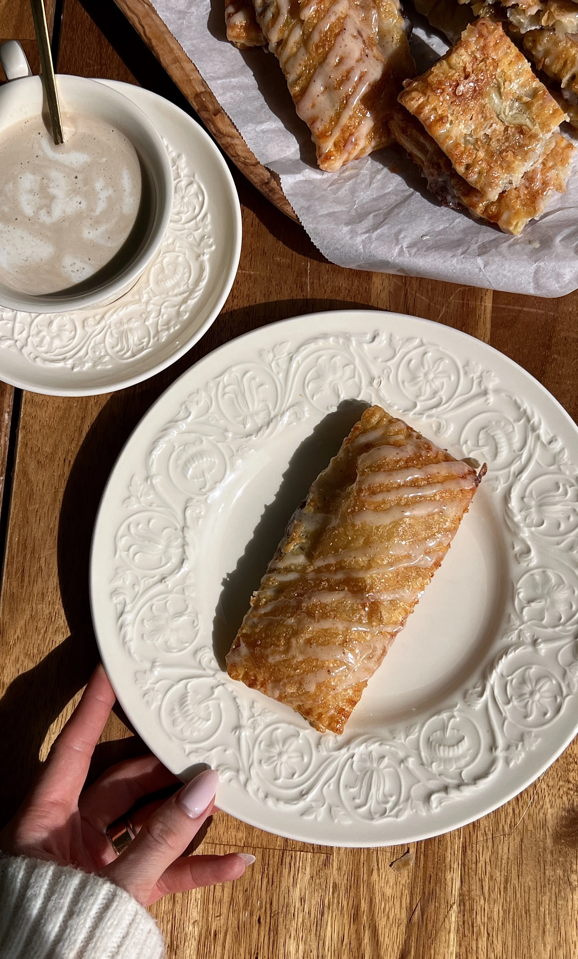 Warm homemade cinnamon roll toaster strudels with brown butter maple cream cheese glaze served with a hot cup of coffee.