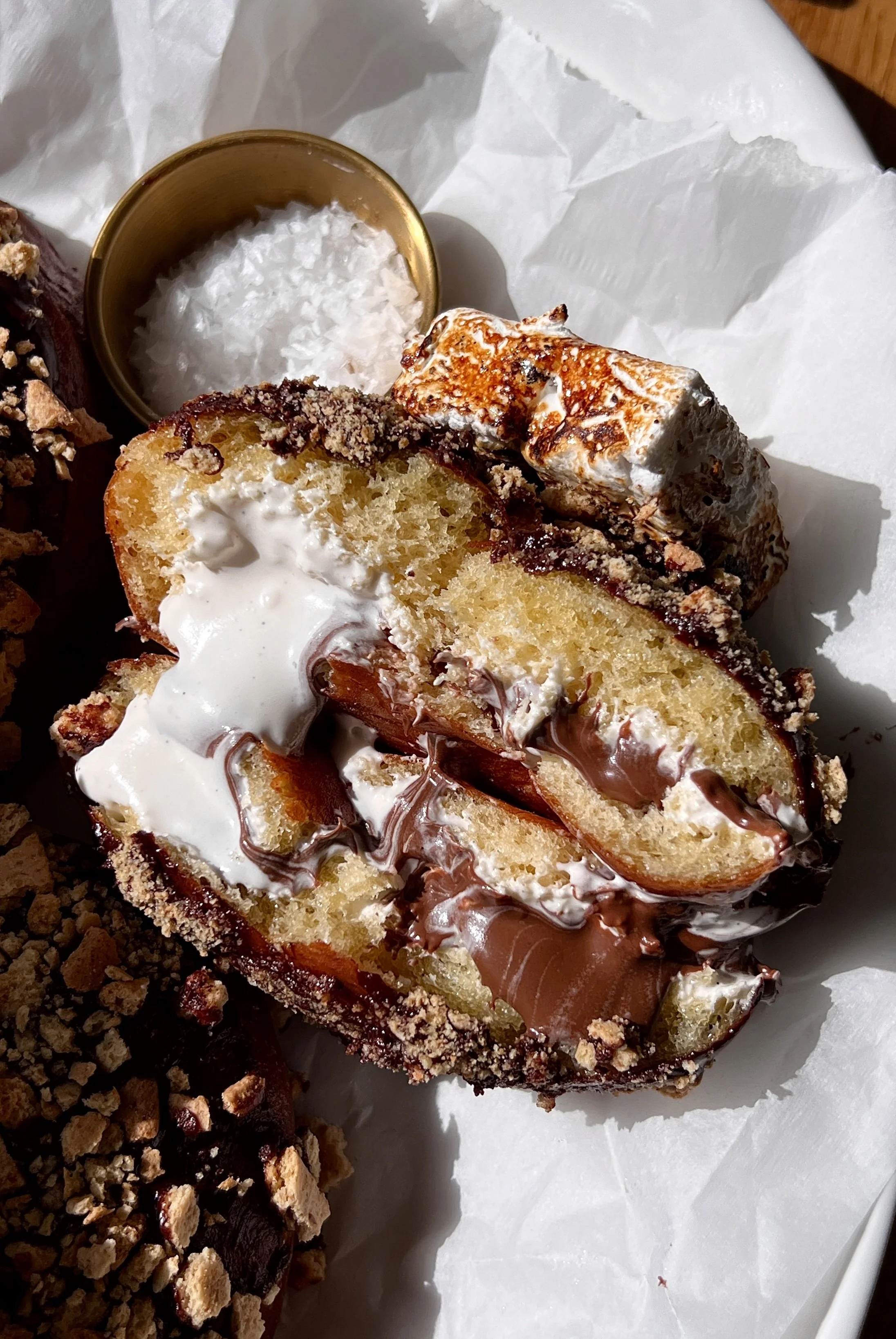 Close-up of a pillowy soft and fluffy s'mores donut with a golden exterior filled with marshmallow buttercream and Nutella finished with chocolate ganache and a toasted marshmallow.