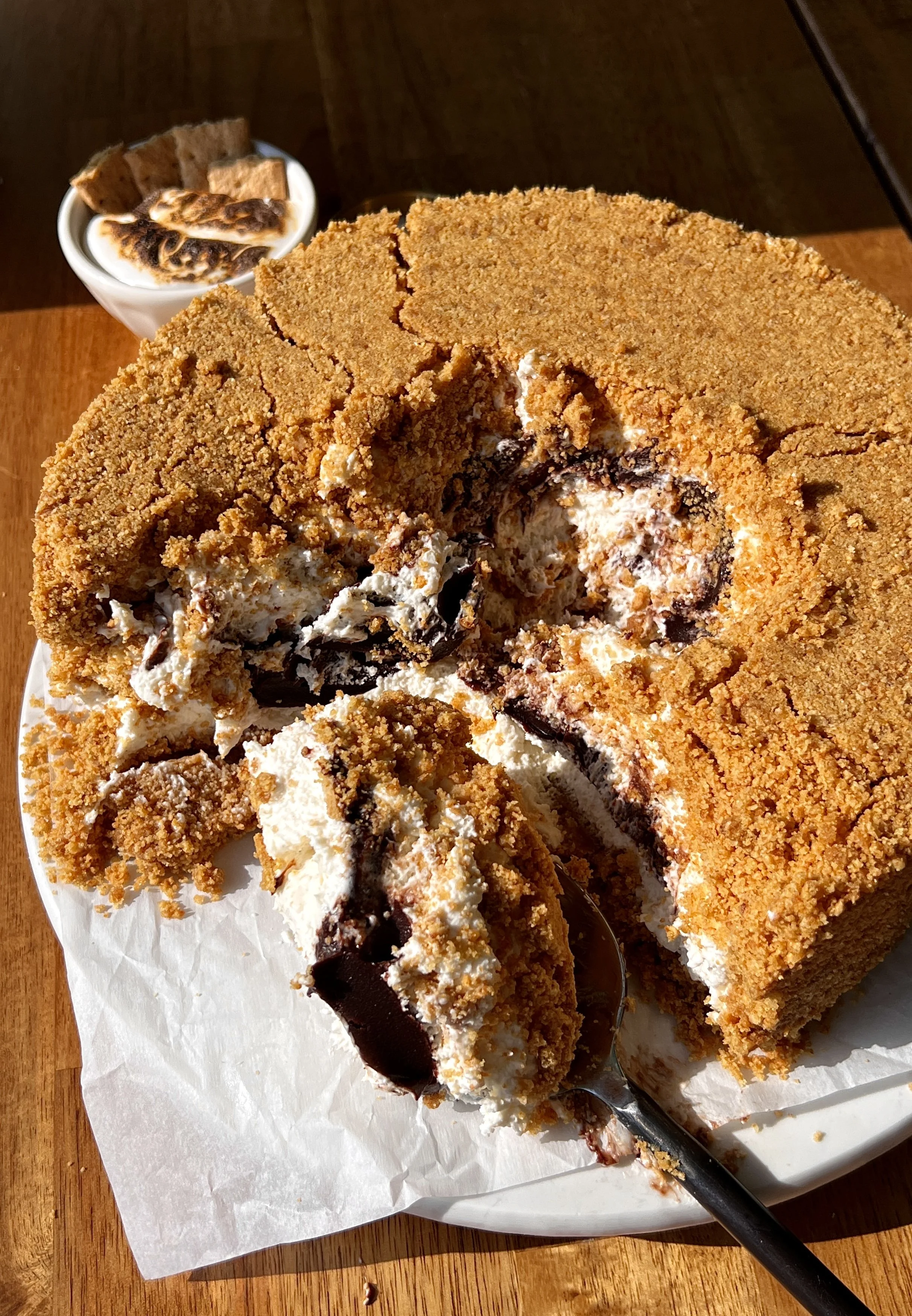 Upside down s'mores cheesecake being smashed into with a spoon revealing the rich and creamy toasted marshmallow cheesecake filling and thick hot fudge sauce inside.