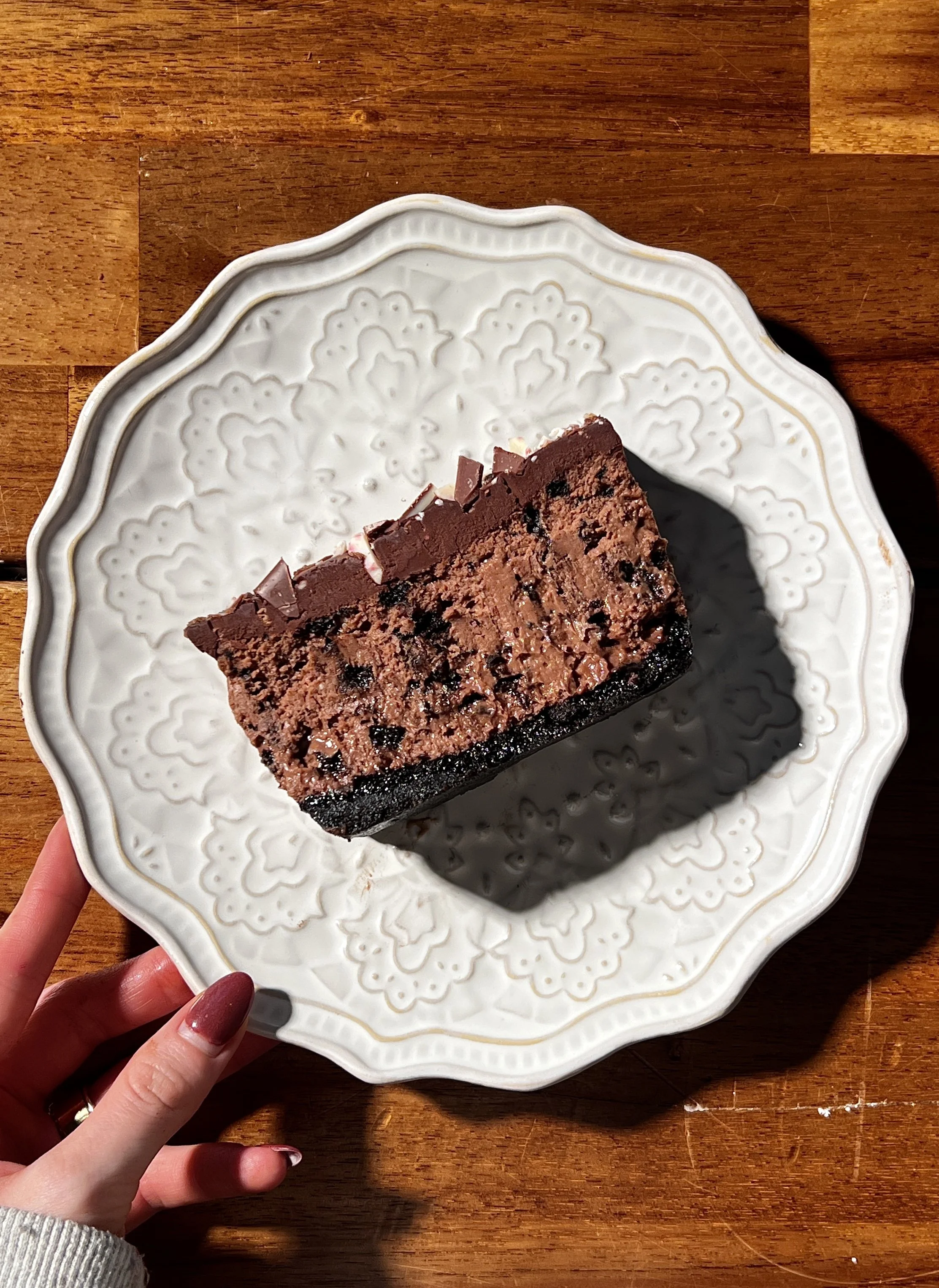 Close-up of peppermint Oreo cheesecake bars with a dark Oreo crust, creamy peppermint mocha cheesecake filling, chocolate ganache topping, and chopped peppermint bark sprinkled on top.