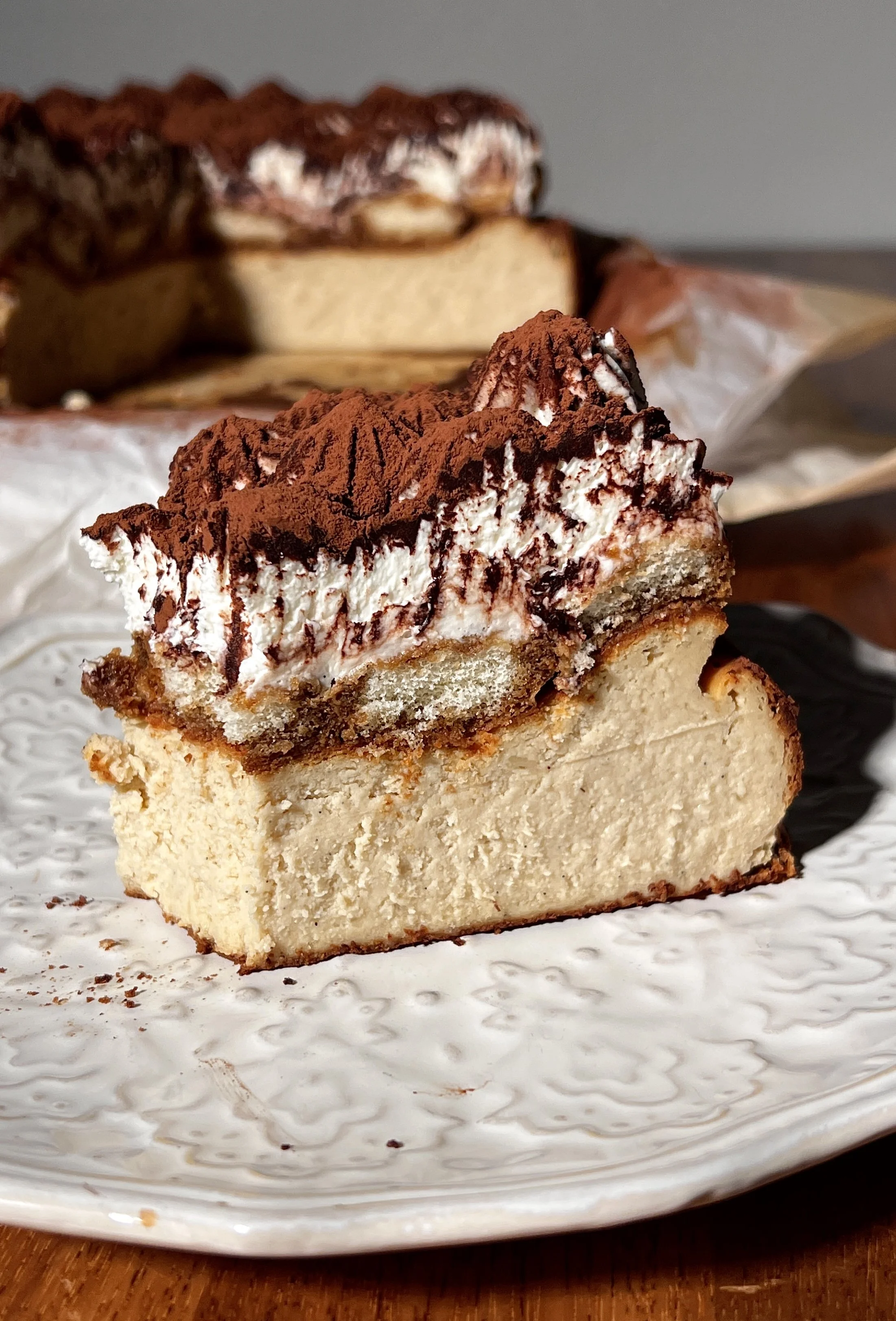Tiramisu basque cheesecake topped with espresso-soaked ladyfingers, creamy mascarpone layer, and a generous dusting of cocoa powder.