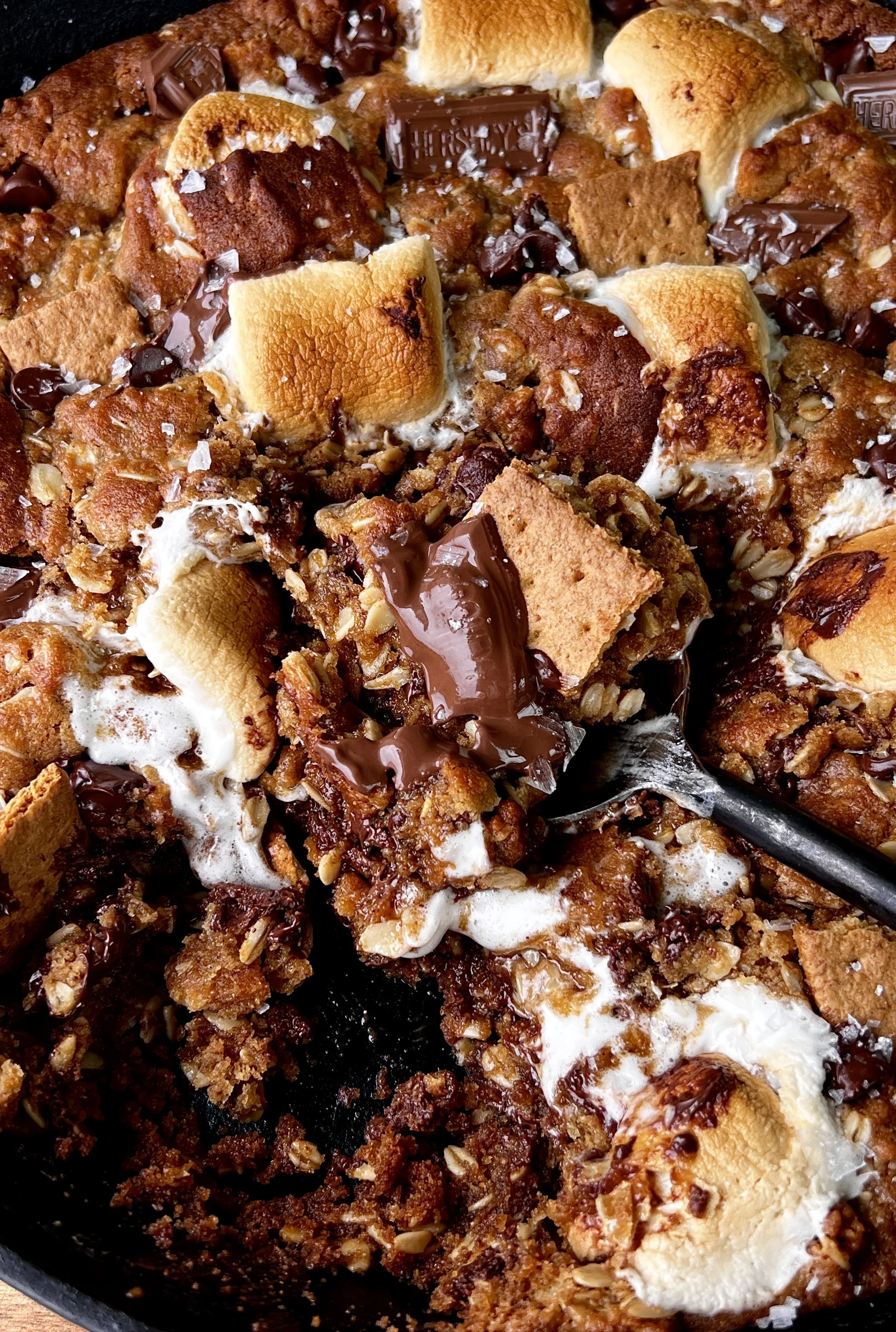 Close-up of a gooey peanut butter s'mores oatmeal cookie skillet with melty chocolate, toasted marshmallows, and crushed graham crackers throughout.