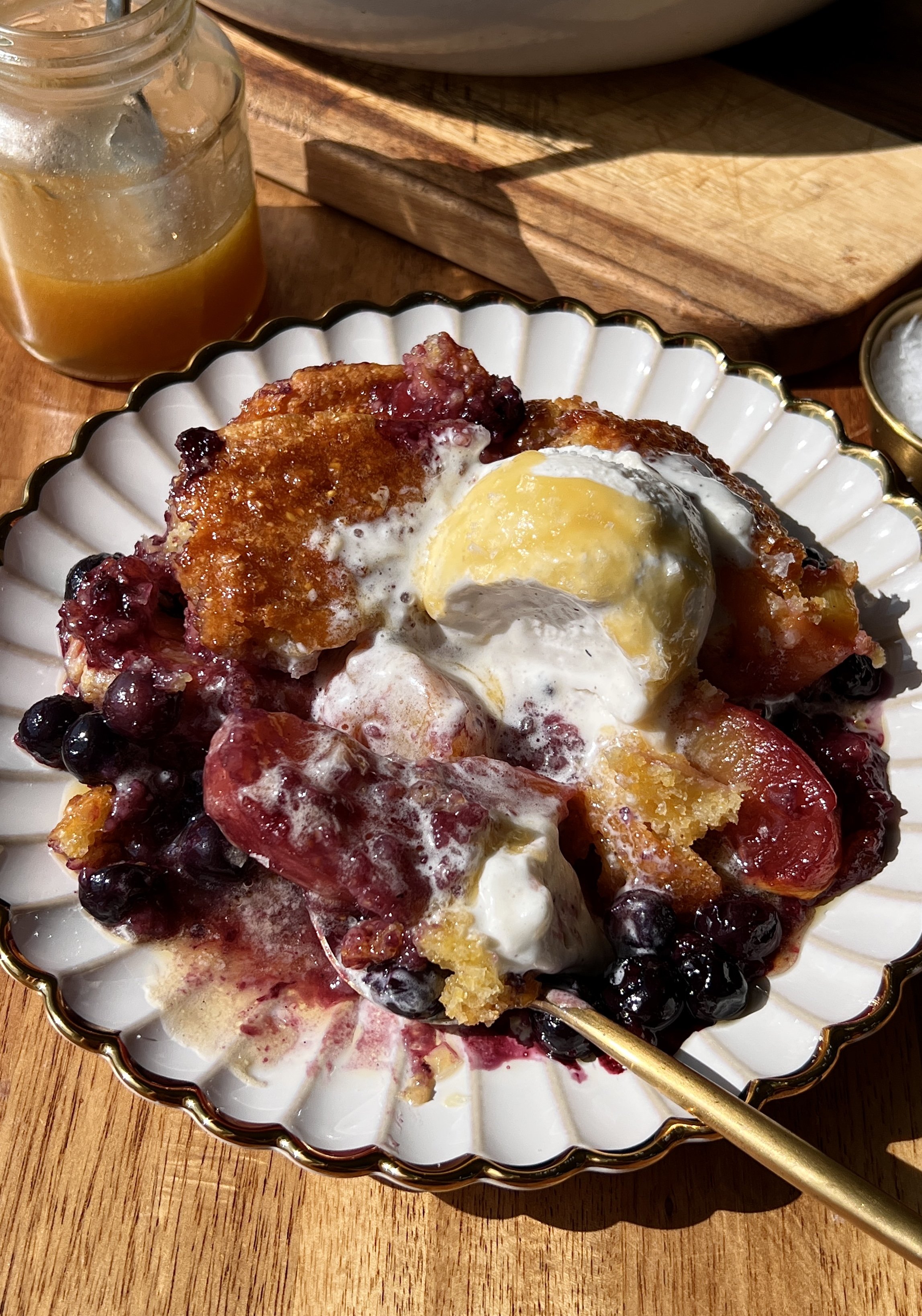 Warm and golden blueberry peach cornbread cobbler brushed with melted honey butter served with a scoop of vanilla ice cream, an extra drizzle of honey butter, and a sprinkle of flaky sea salt as the ultimate summer dessert.