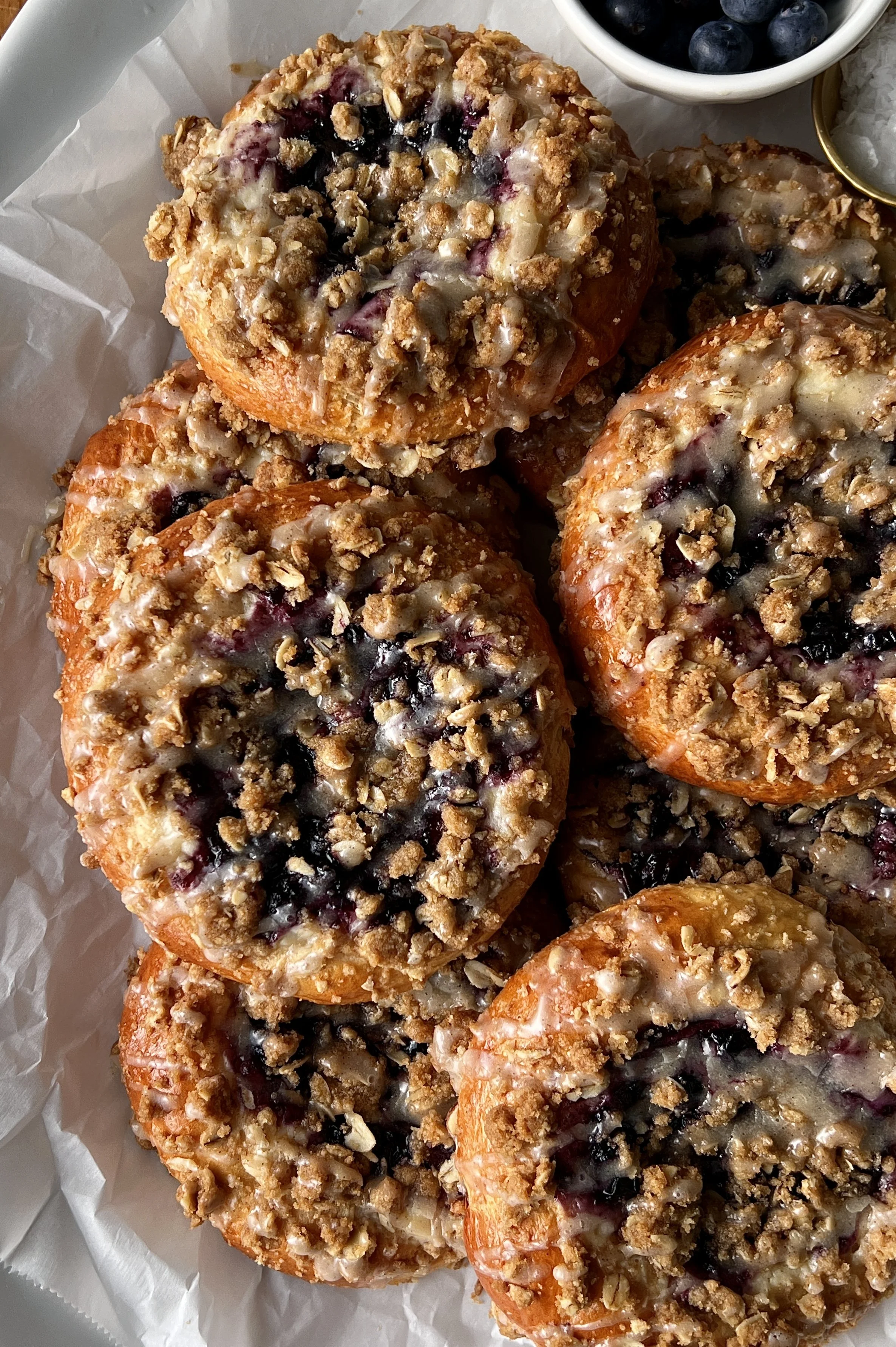 Close-up of a soft and pillowy blueberry cheesecake streusel bun with a rich and tangy cheesecake filling, homemade jammy blueberry compote, and golden oat streusel throughout.