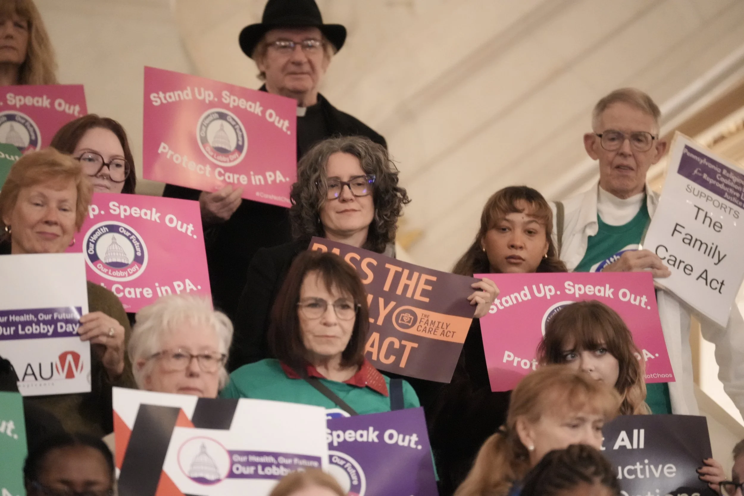 A group of people holding signs that say "Protect Care in PA"