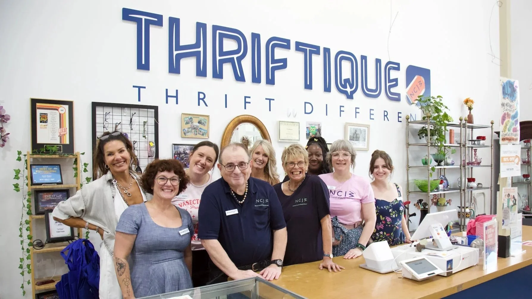 A group of smiling people standing in from of a sign that says "Thriftique"