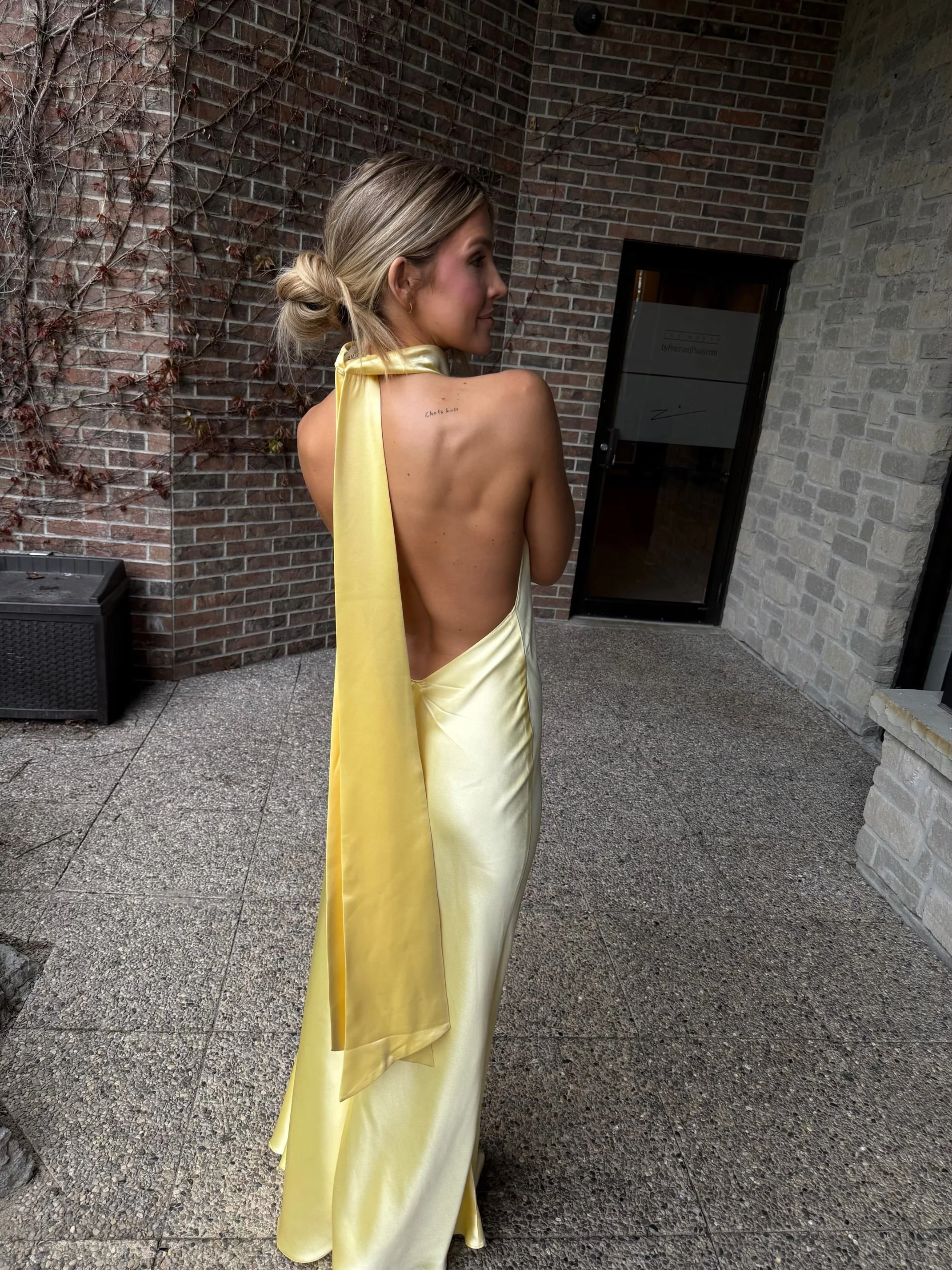 Wedding guest or bridesmaid wearing a backless yellow satin dress showcasing a natural custom spray tan by Schulz Beauty in Toronto