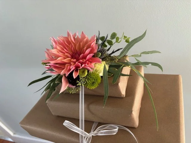A bouquet of pink, green, and yellow flowers on top of wrapped gift boxes with a ribbon bow.