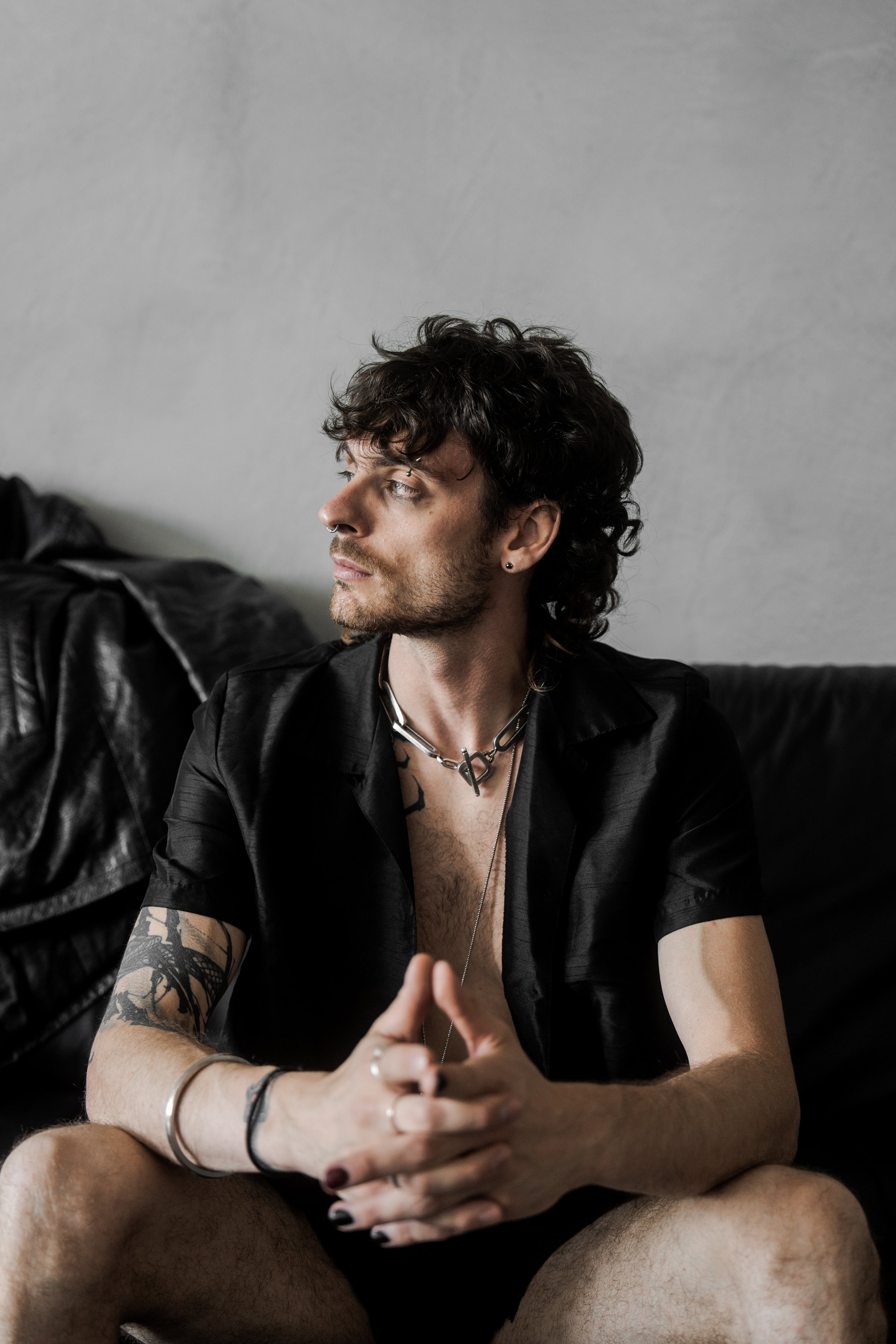 XINIX sitting in low light wearing open shirt with dark moody cinematic aesthetic