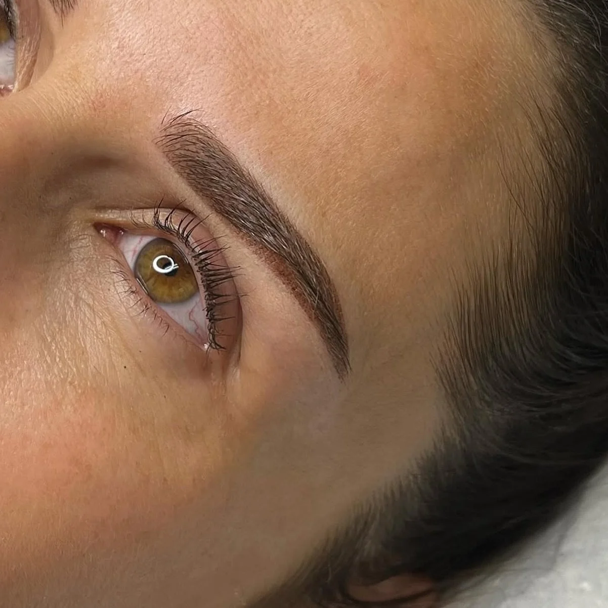 Zoom sur un œil humain avec sourcils bien définis, peau claire et cheveux foncés. La personne a des cils longs et une pupille marron.