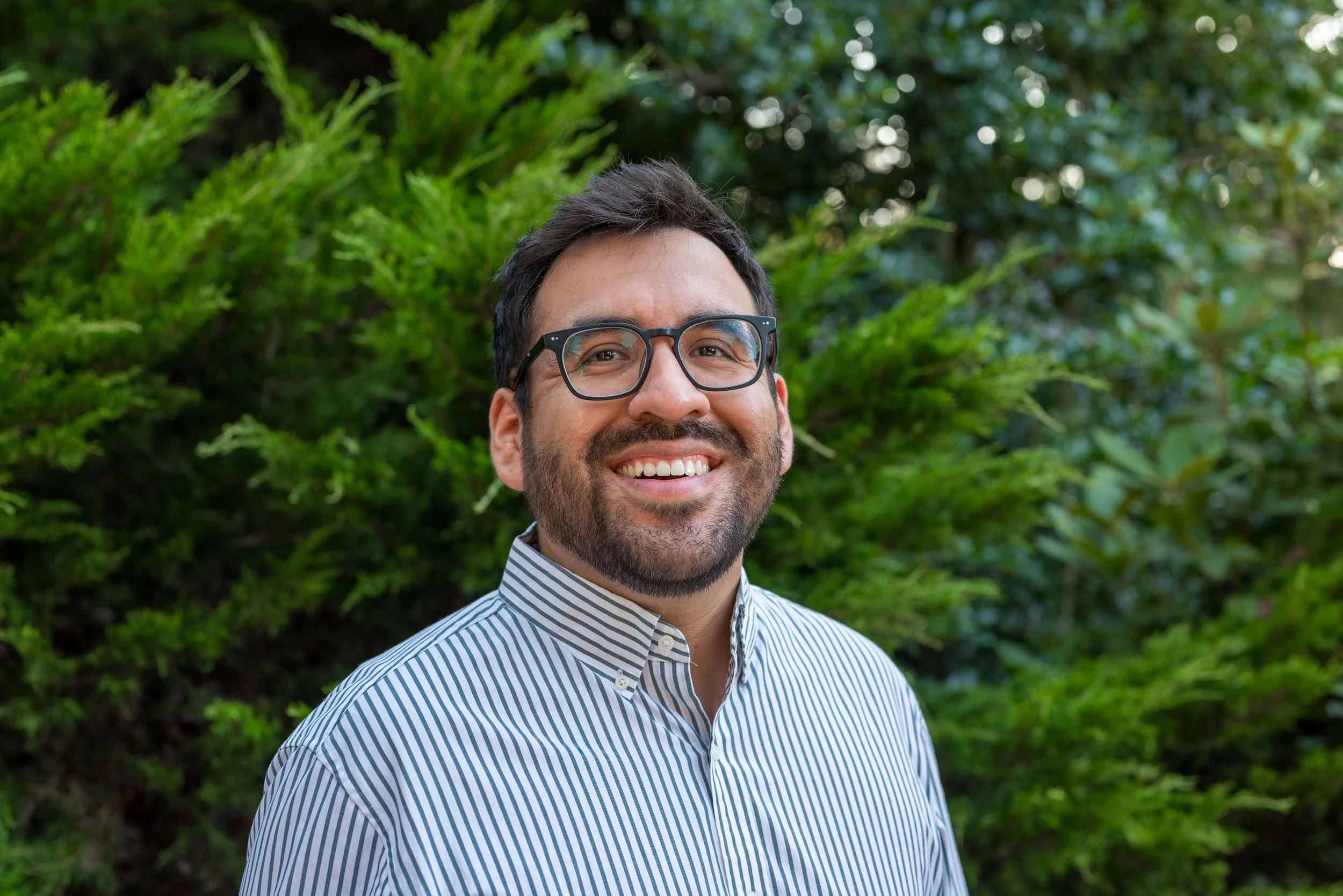 Smiling man wearing glasses and a black shirt against a dark background.