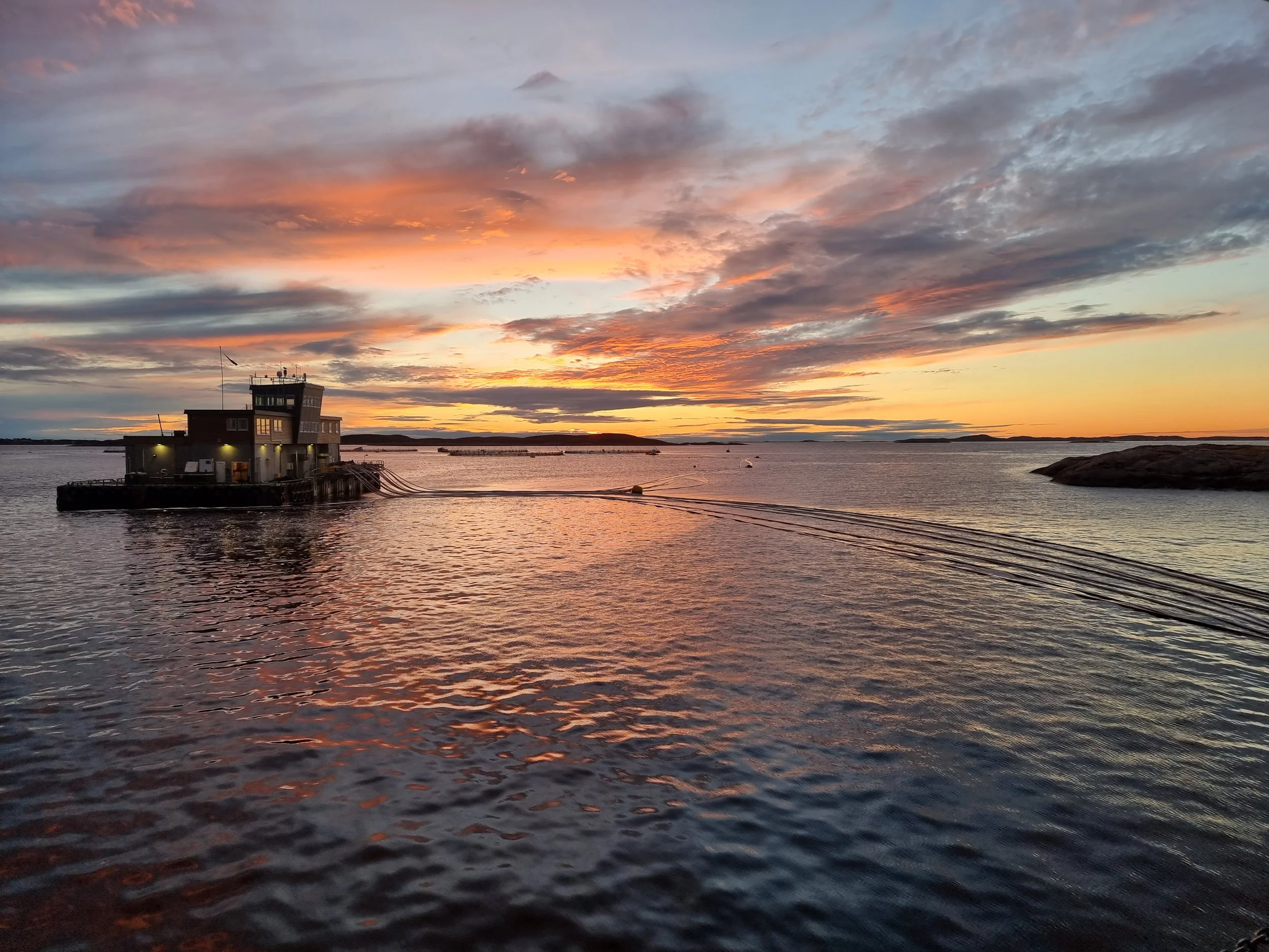 A boat on calm water during a colorful sunset with pink, orange, and purple clouds.