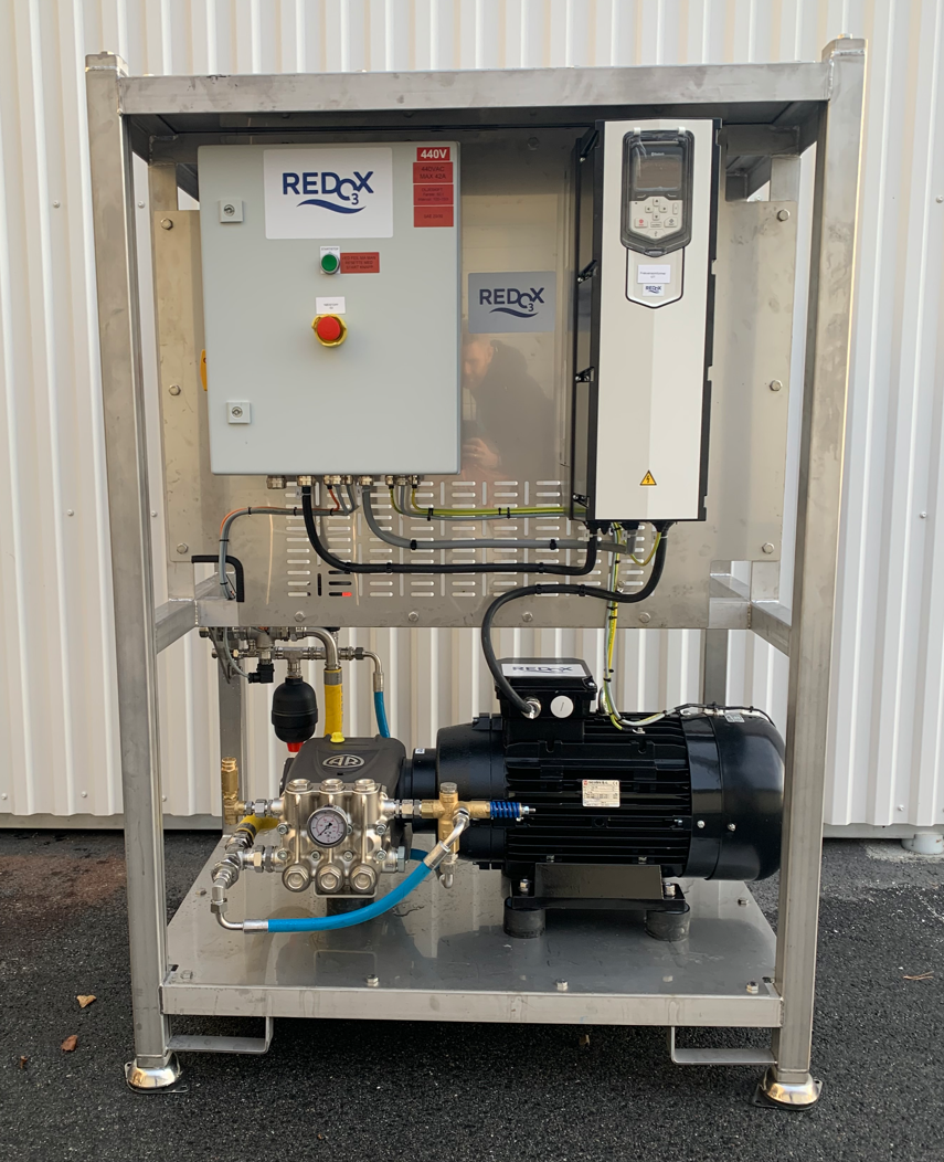 Industrial equipment with a control panel, motor, and piping, mounted on a metal frame outside a building.