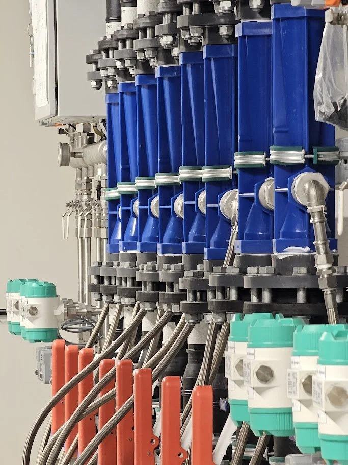 Industrial machinery with multiple blue, green, and orange components connected by stainless steel pipes and fittings.