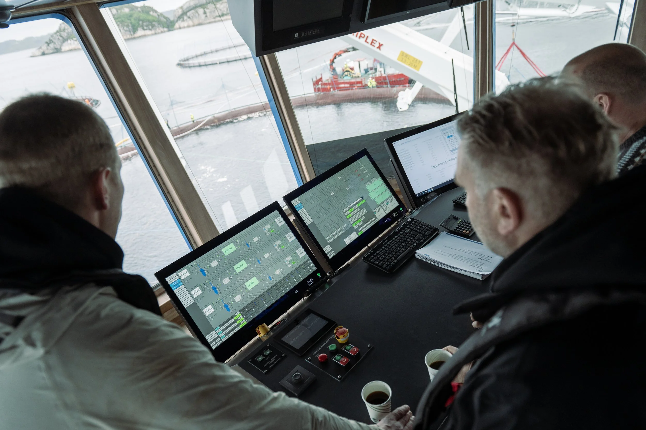 Ship crew inside the bridge navigating the vessel with multiple computer screens displaying navigation data.