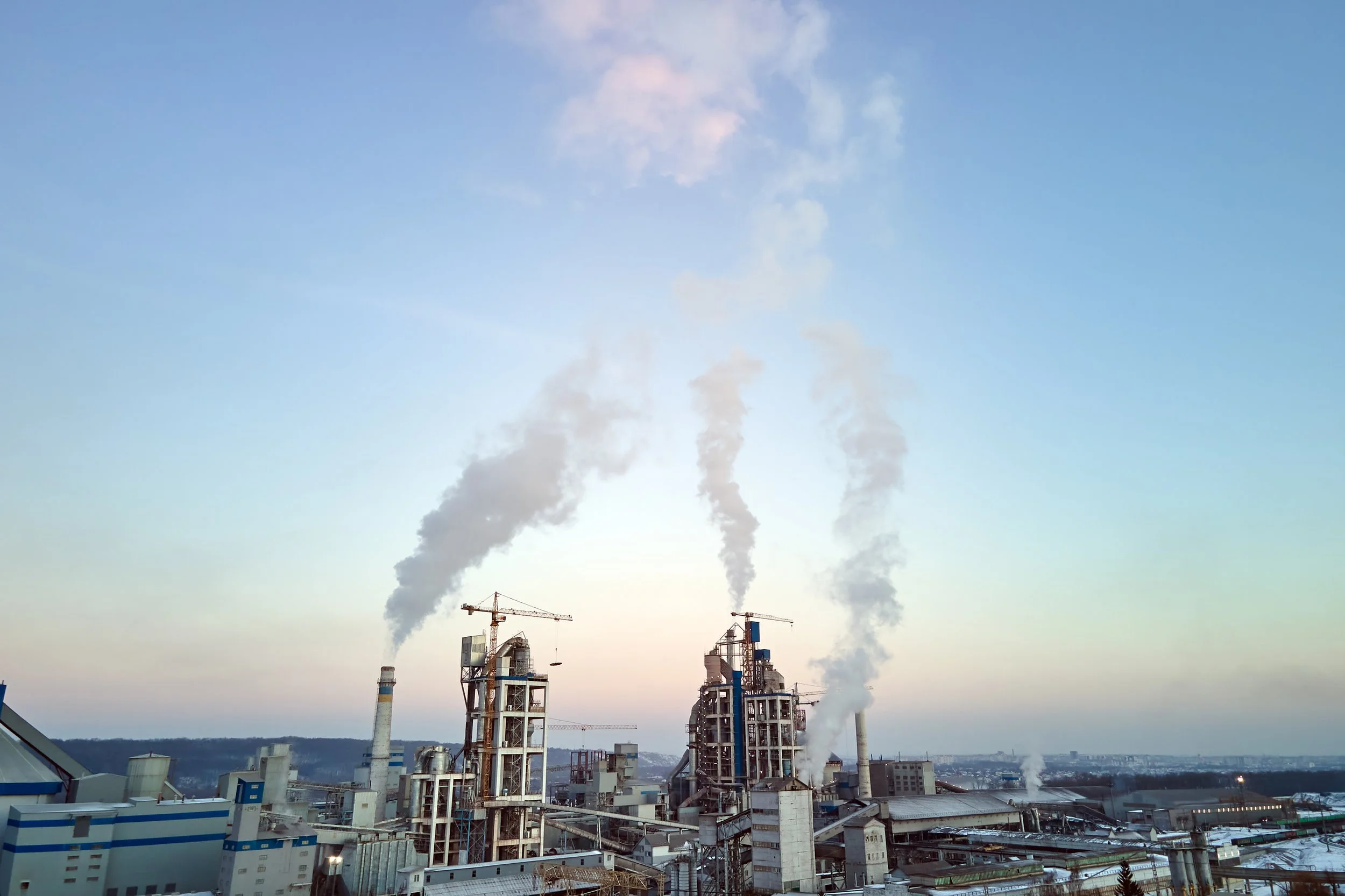 Industrial factory with multiple chimneys emitting smoke, under a partly cloudy sky.