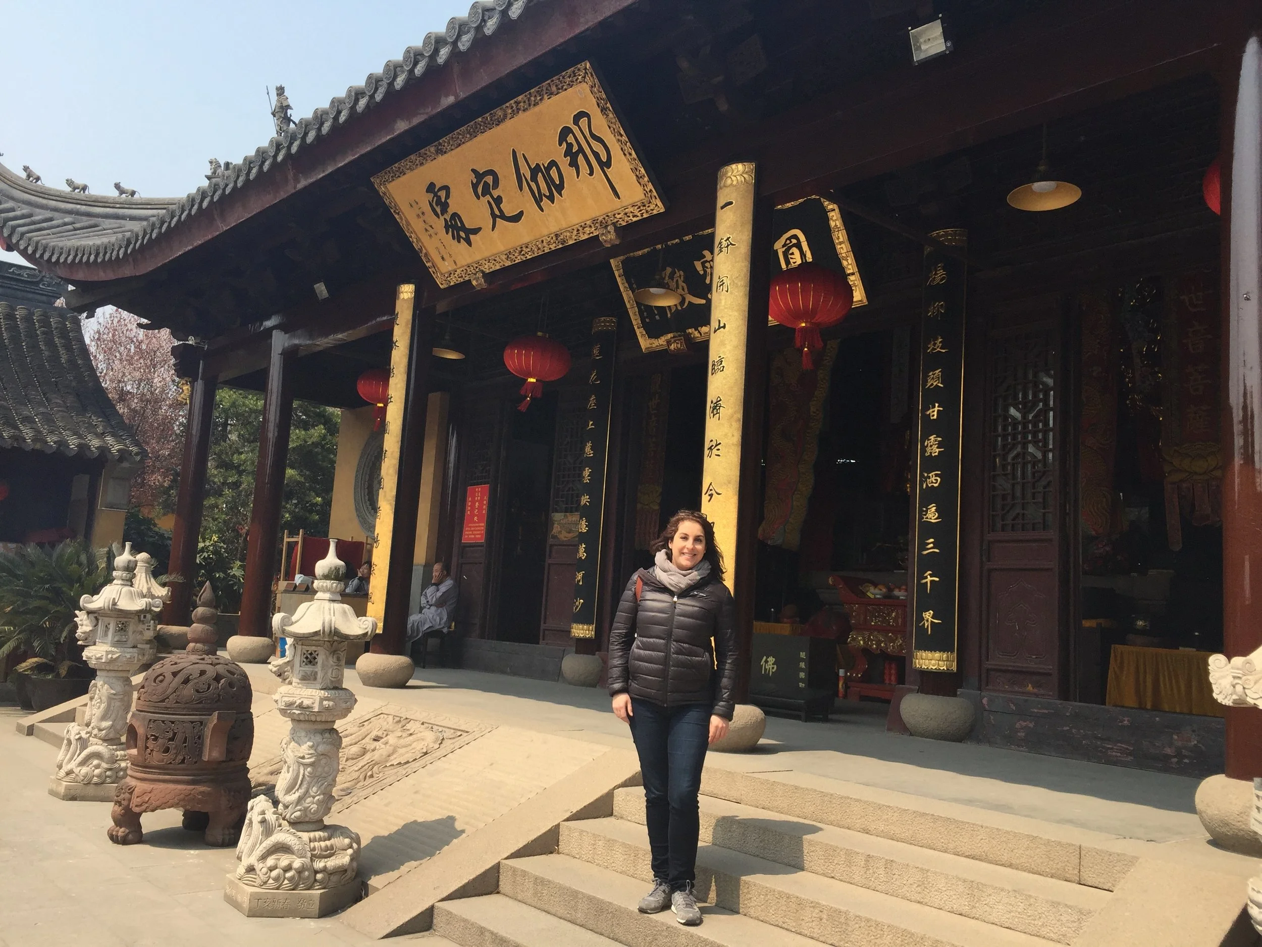 Femme devant un temple taoiste chinois traditionnel avec lanternes rouges et décorations en bois, ascendant des marches en pierre.