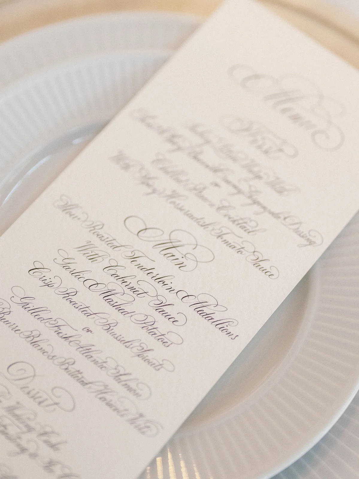 Close-up of a white, elegant printed menu or program with cursive text, placed on a white plate or tray.