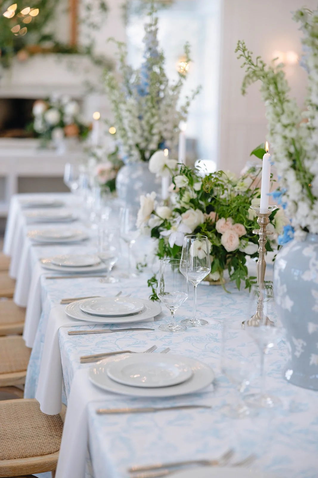 Elegant banquet table setting with white tablecloth, white china plates, wine glasses, silverware, floral centerpieces with white and pink flowers, and tall white candles in silver holders, decorated for a formal event.