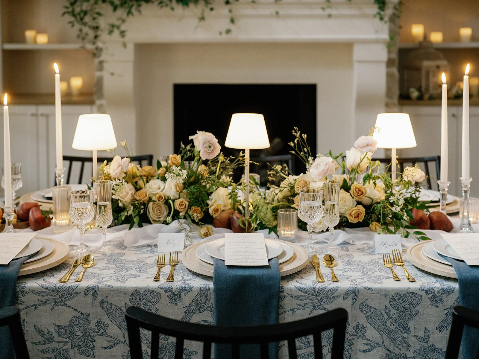 Elegant dining table decorated with floral arrangements, candles, and tableware in a cozy room with a fireplace.