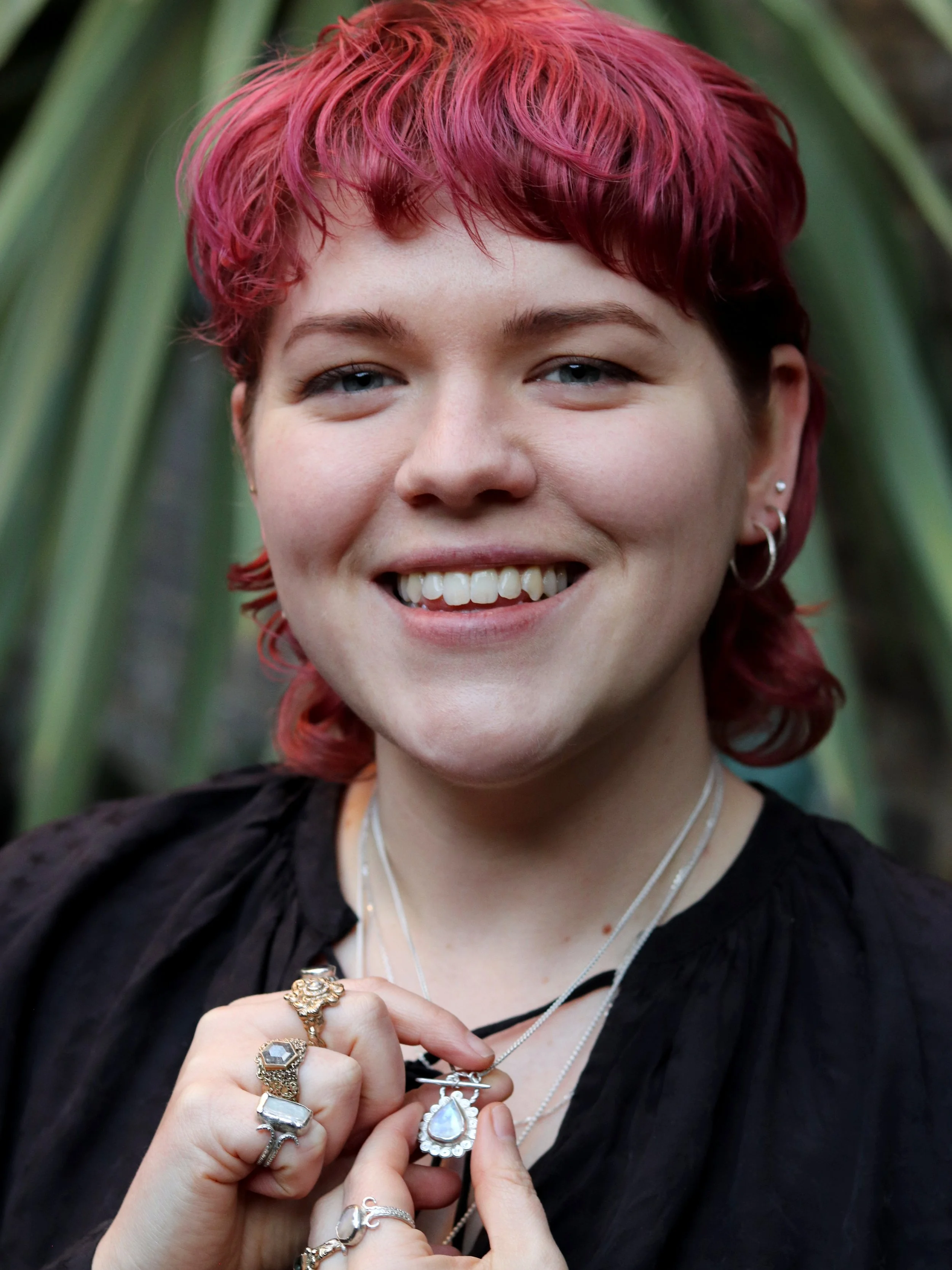 photo of a person with white skin and bright pink hair, holding up a silver necklace and smiling