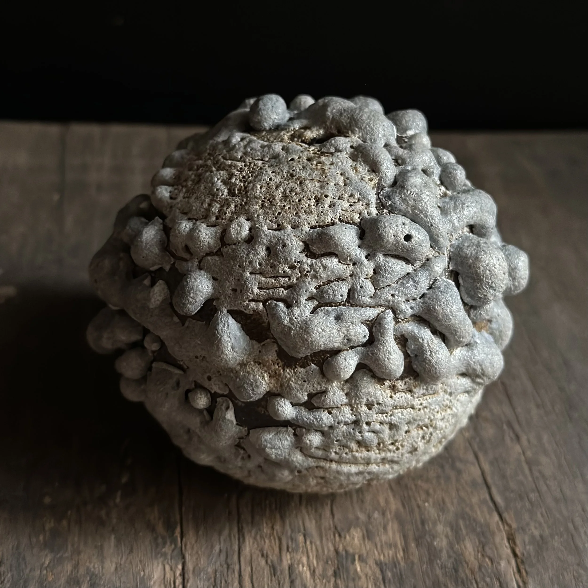 Round vessel covered in lava glaze bumps like barnacles, on wood