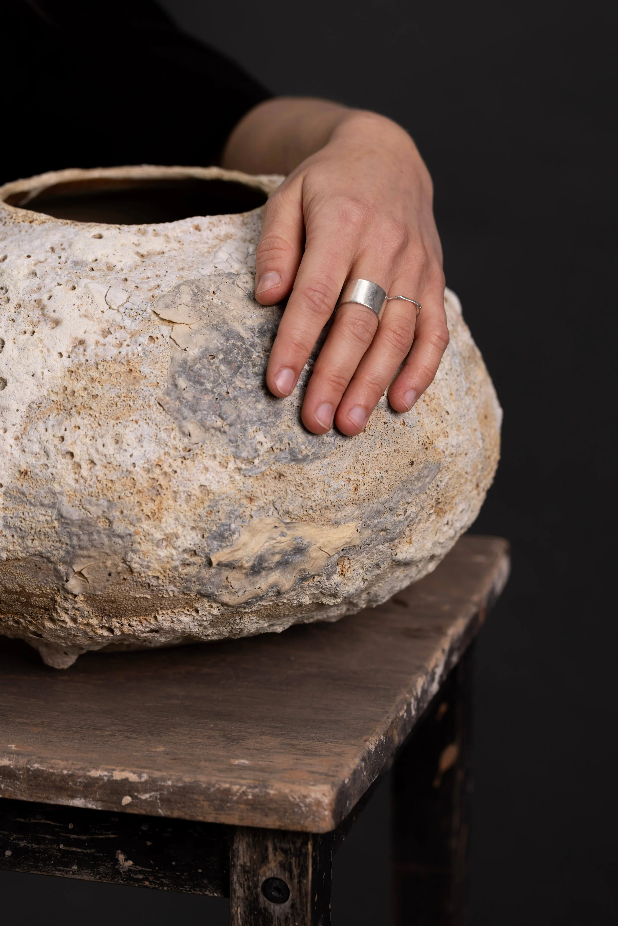 Artist's hand resting on large irregular cream vessel with pumice/crater texture
