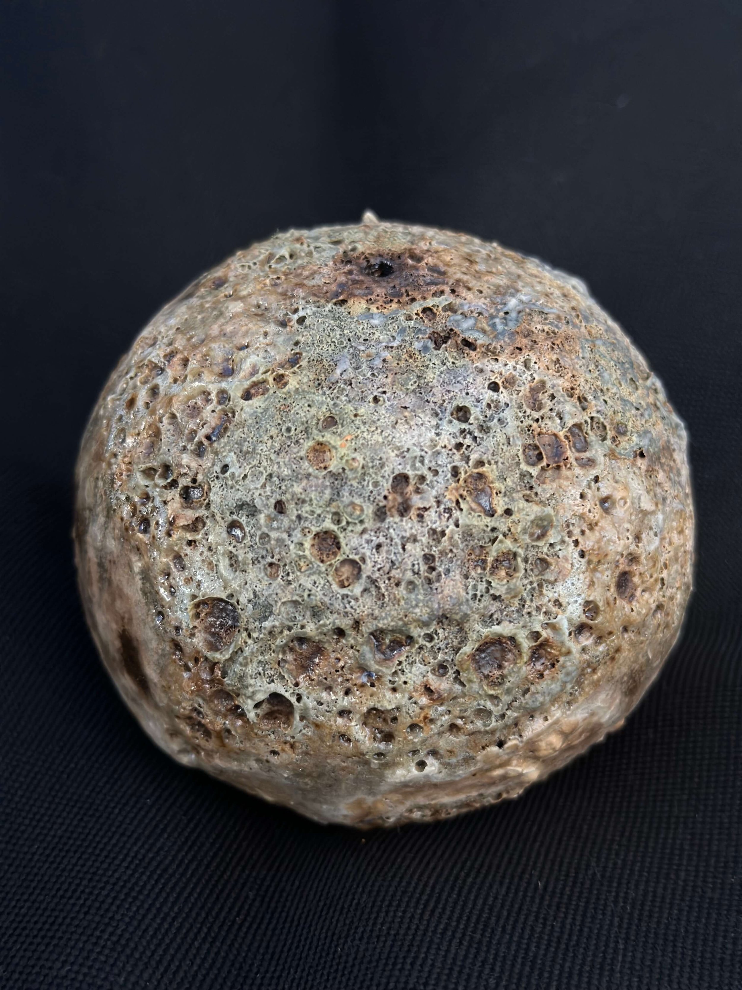 Flat round ceramic puck with heavily cratered lava glaze