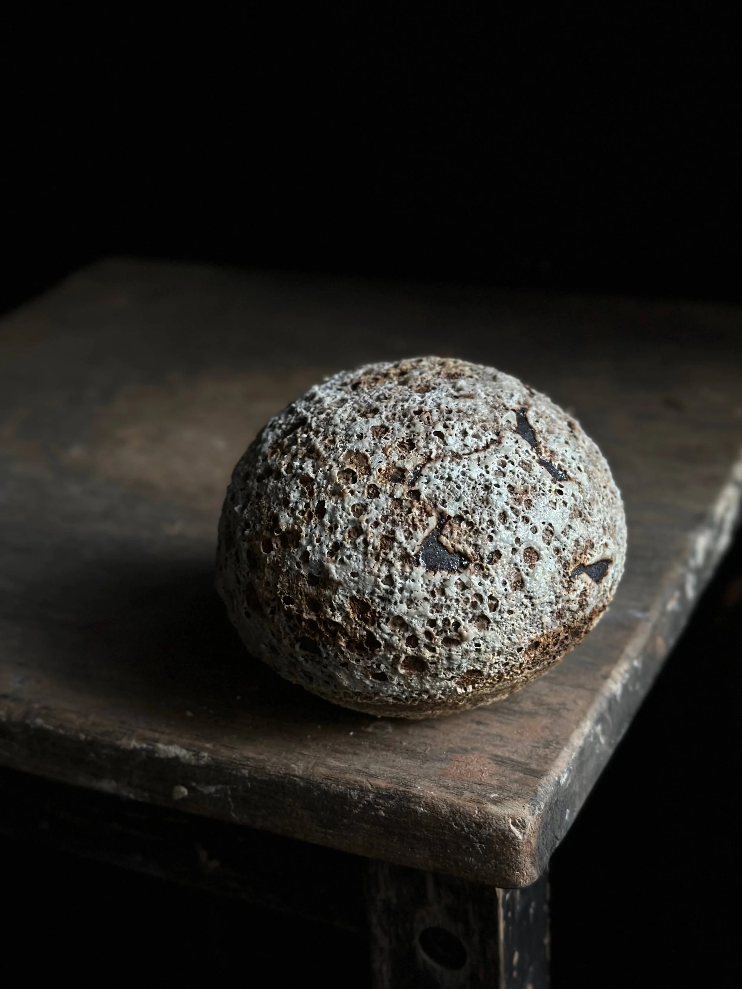 Dark gray/black round vessel with volcanic crater glaze on wood