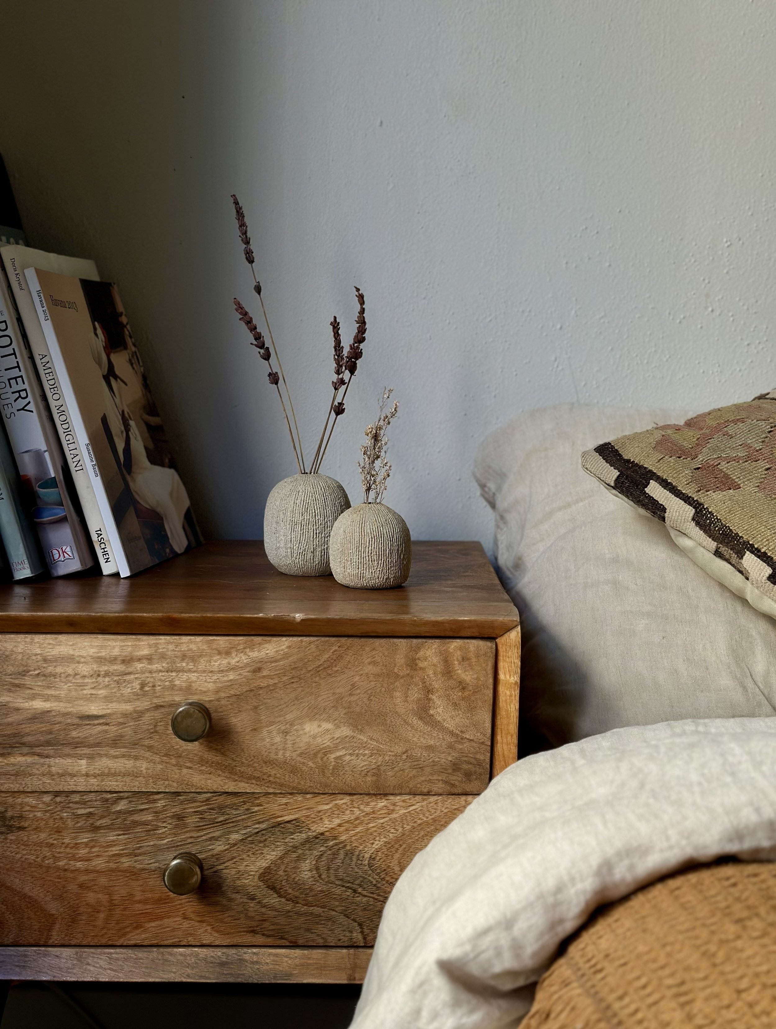Two small textured bud vases with dried lavender on a wooden bedside table