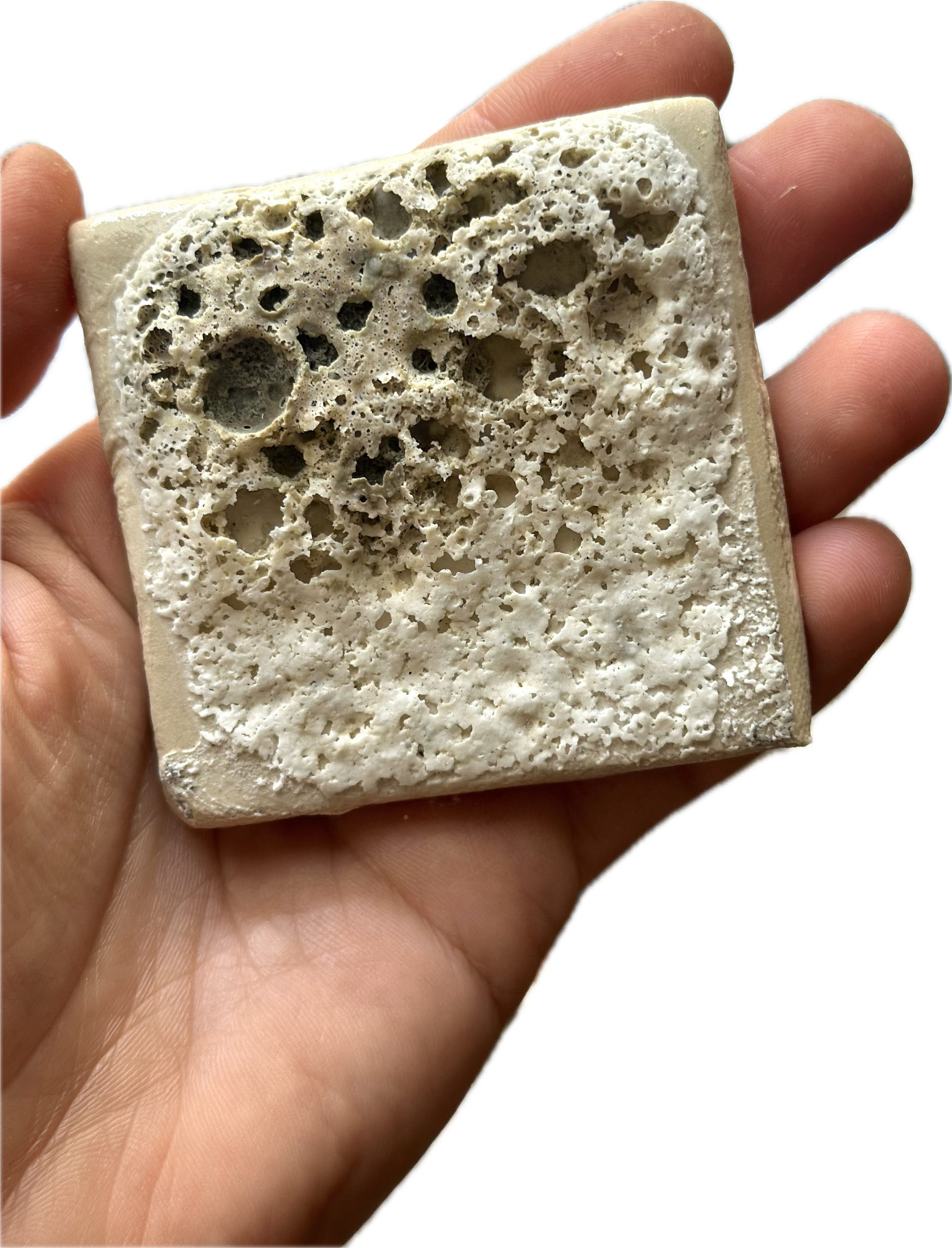 Close-up of a hand holding a square piece of pumice stone with a rough, porous surface.