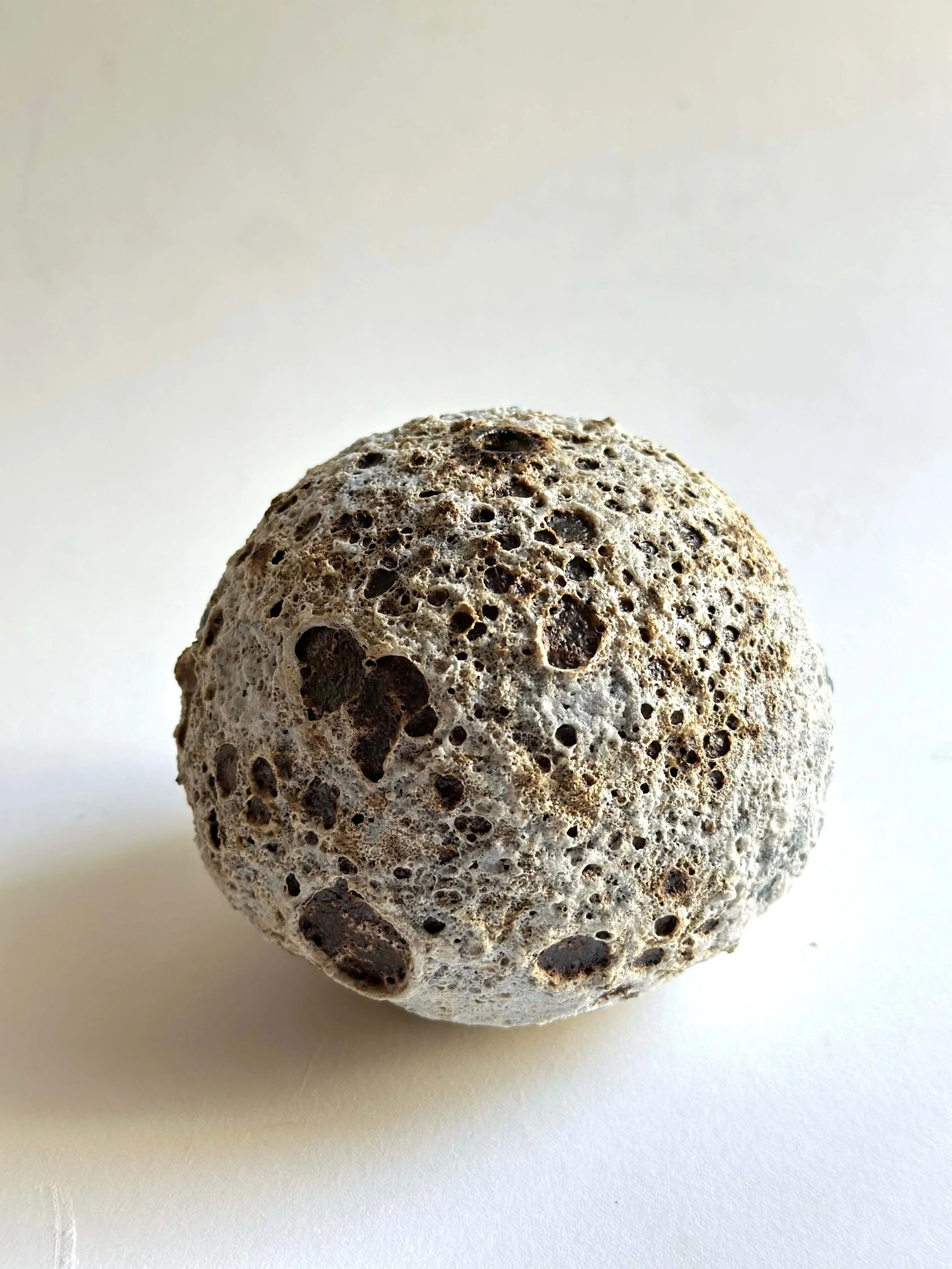 Close-up of a little vase with dark specks on a white surface.