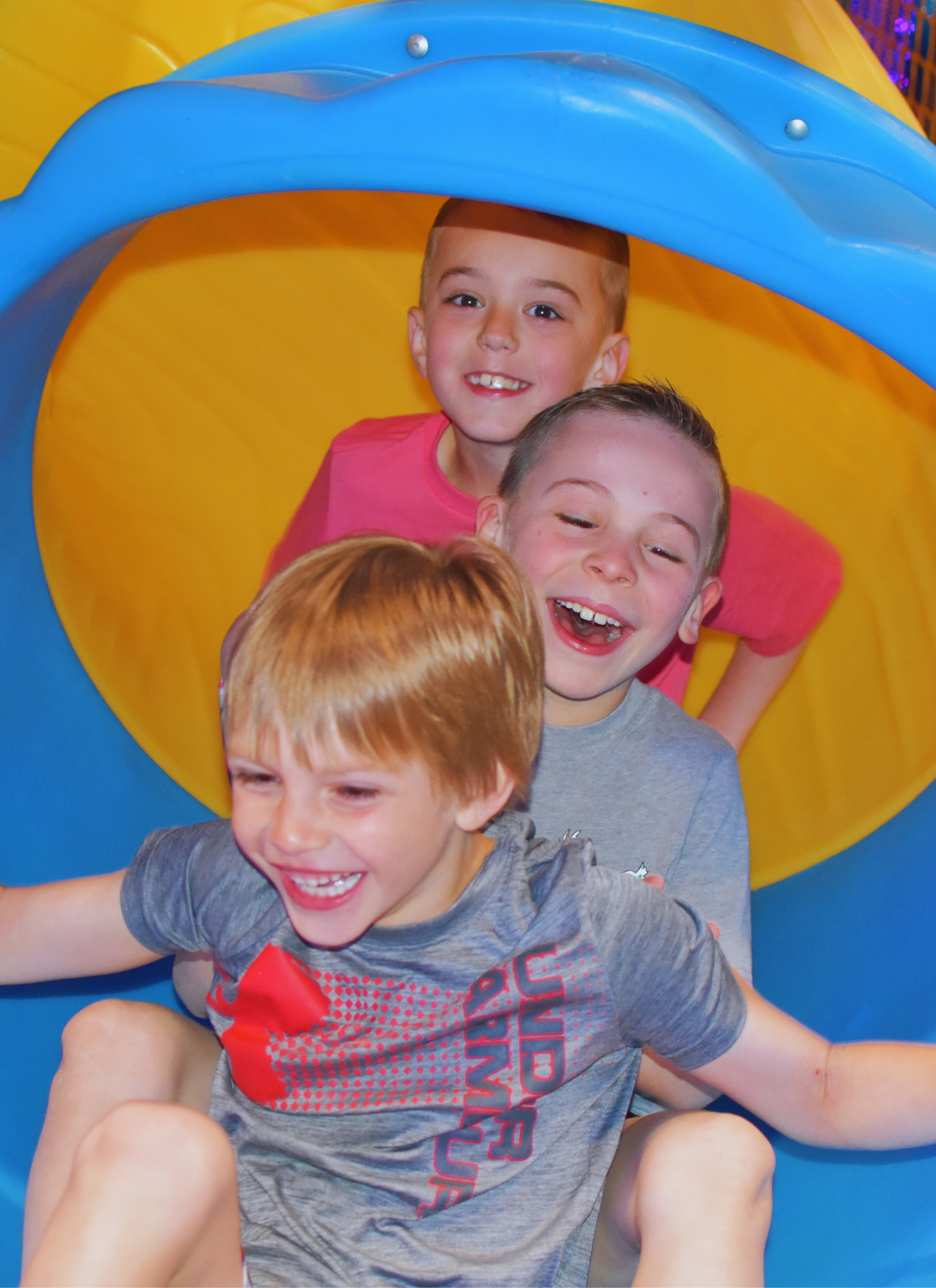 Three young boys sliding down a colorful playground slide, laughing and enjoying themselves.
