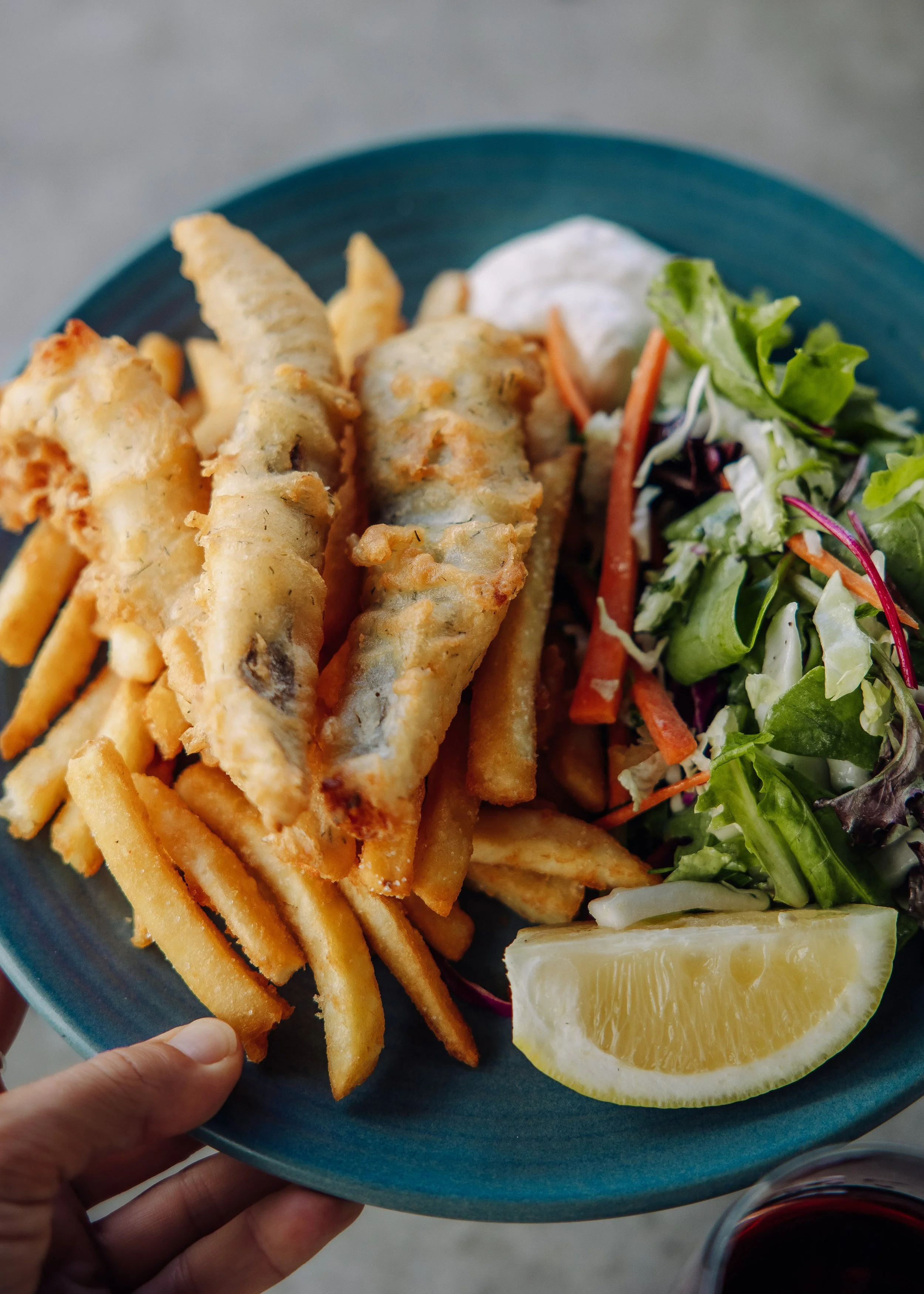 A plate with battered fish, hot chips, a side salad with mixed greens, shredded carrots, and a lemon wedge.