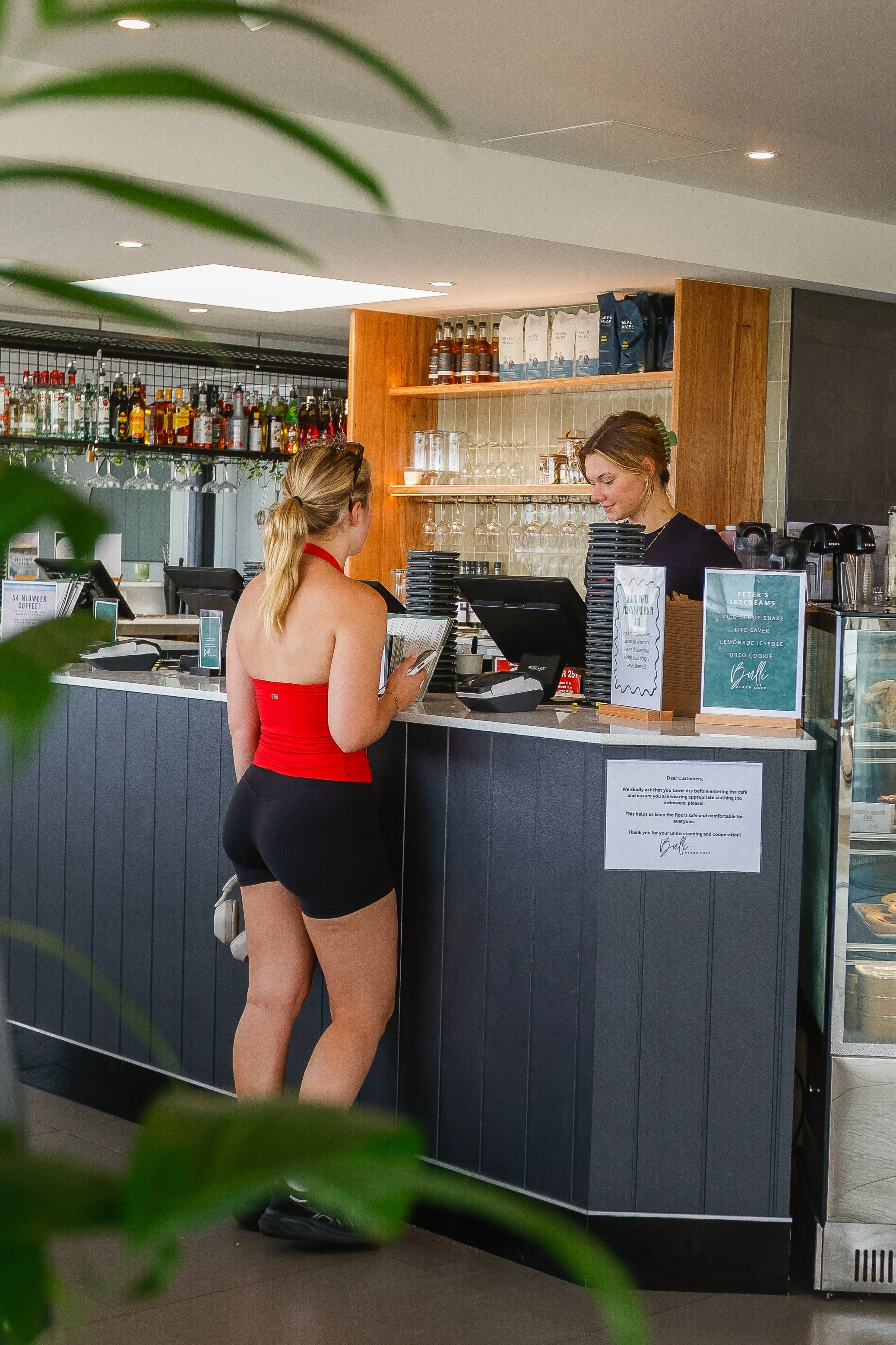 A woman in athletic wear at a cafe counter, placing an order with a staff member behind the counter.