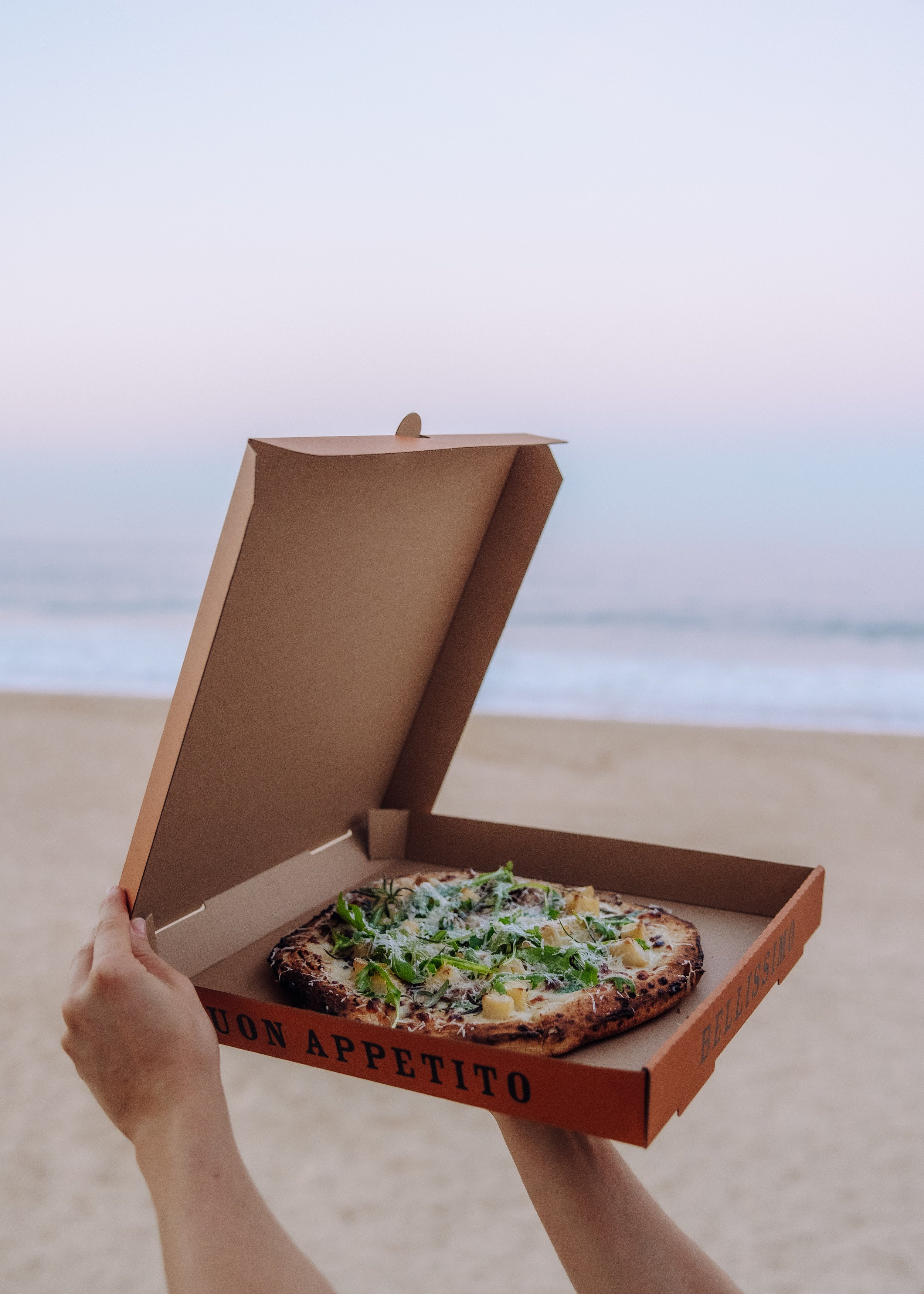 A person holding a takeaway pizza box with a wood-fired Potato pizza