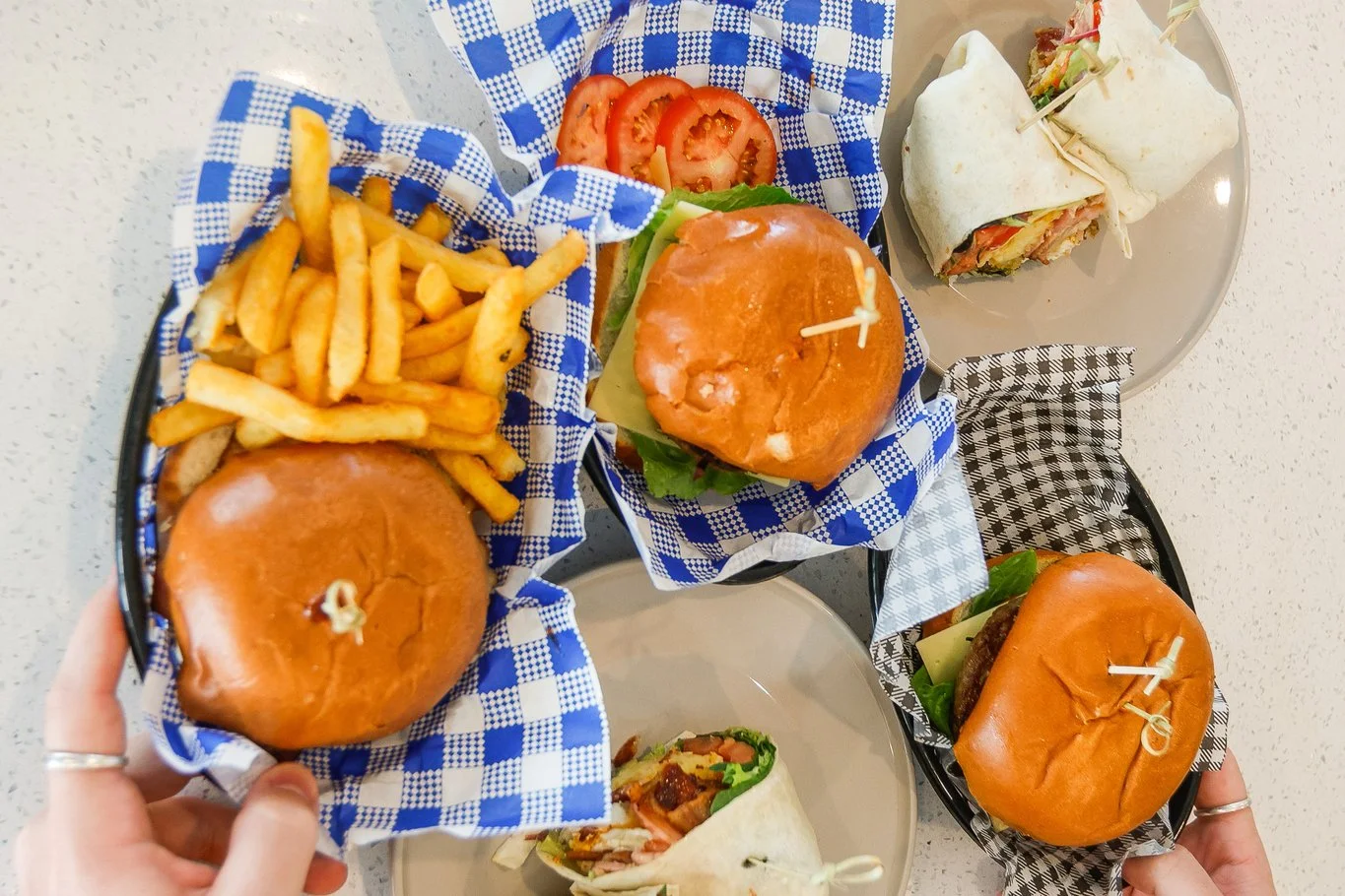 Three plates with a breakfast burger, chicken burger, beef burgers, fries, and breakfast wraps on a white table.