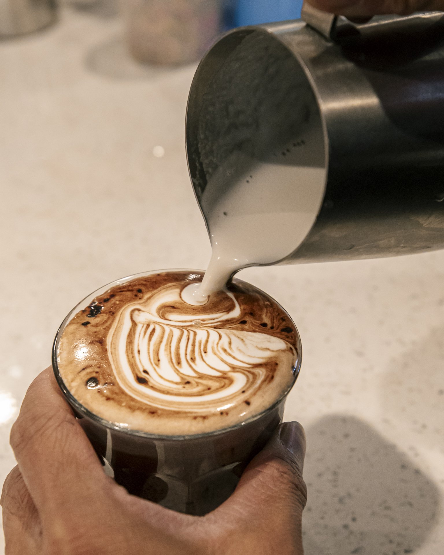 Skilled barista creating swan latte art while pouring coffee made with Seven Miles Coffee beans at a coastal cafe