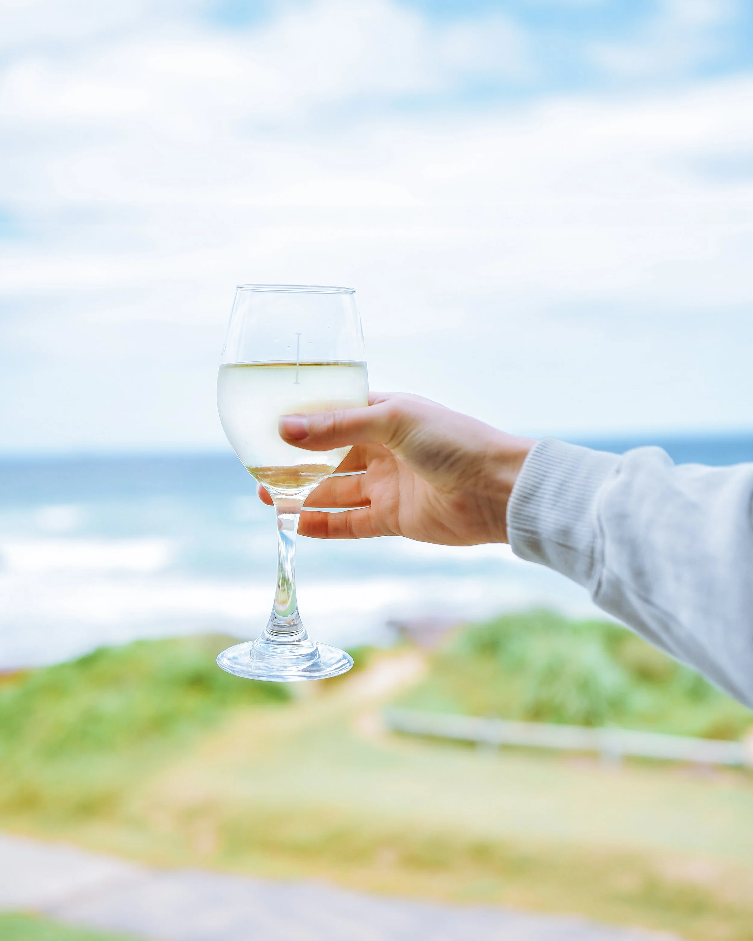 Person holding a glass of white wine outdoors near the seaside.