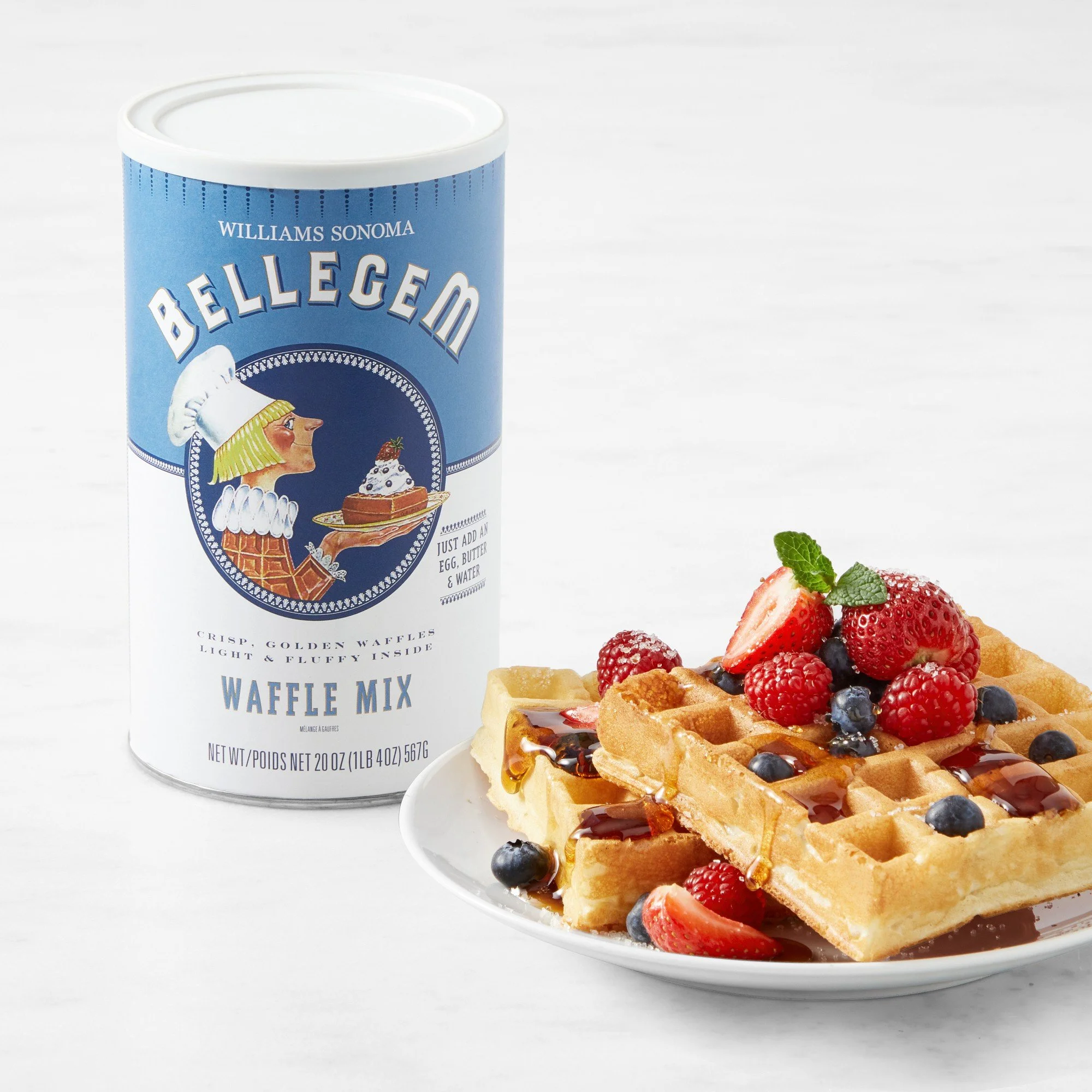 A plate of waffles topped with fresh berries, mint, and syrup next to a container of waffle mix powder.
