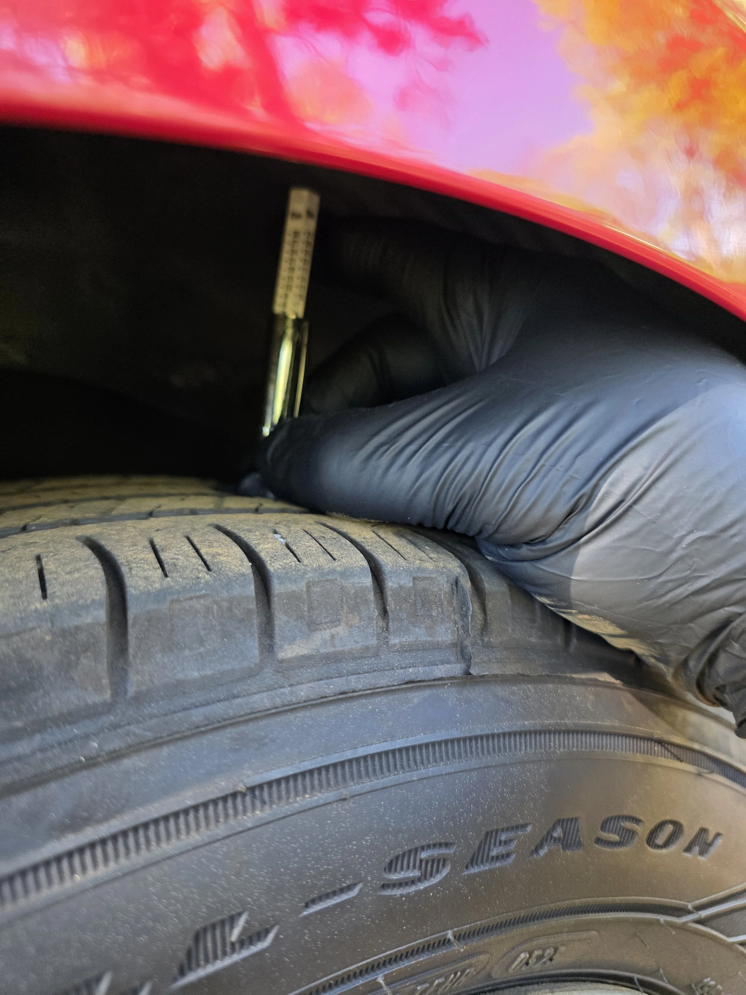 A person wearing a black glove measuring the tread depth of a tire with a tire tread depth gauge.