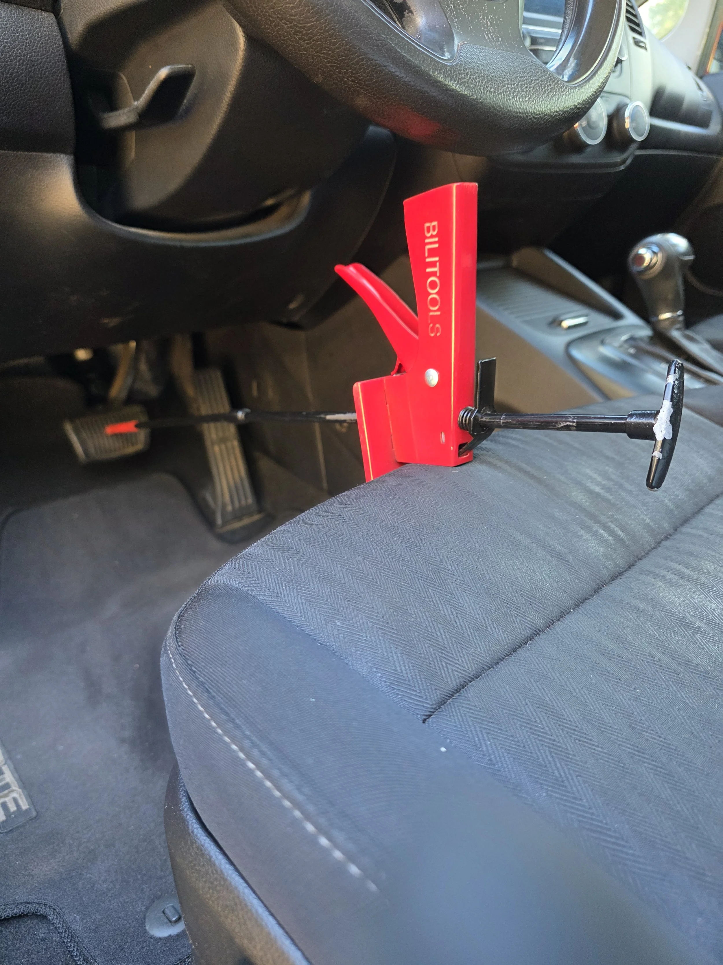 A red BilTools pry bar with a black handle resting on a car seat, inside the vehicle's interior.