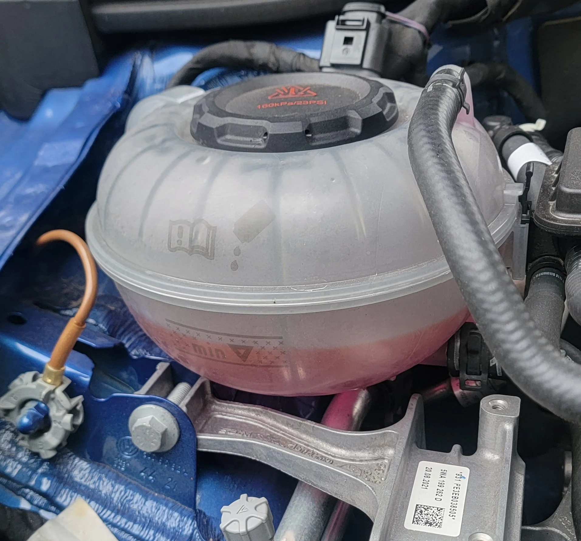 Car engine with coolant reservoir tank partially filled with pink coolant.