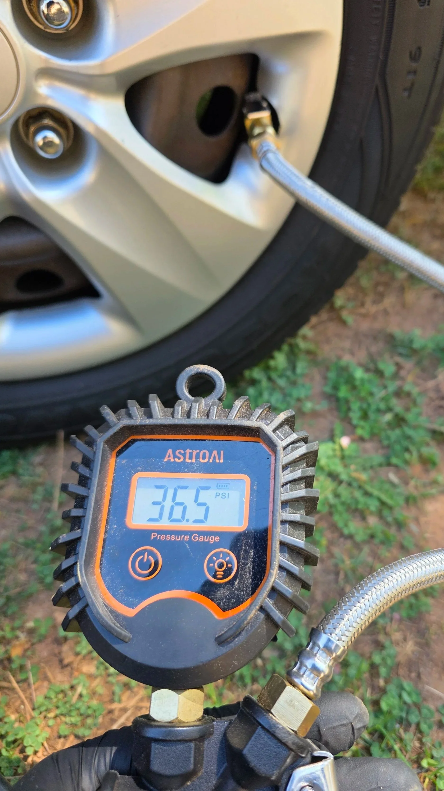 A digital pressure gauge showing 36.5 PSI attached to a tire's valve stem, with an air hose connected to inflate the tire.