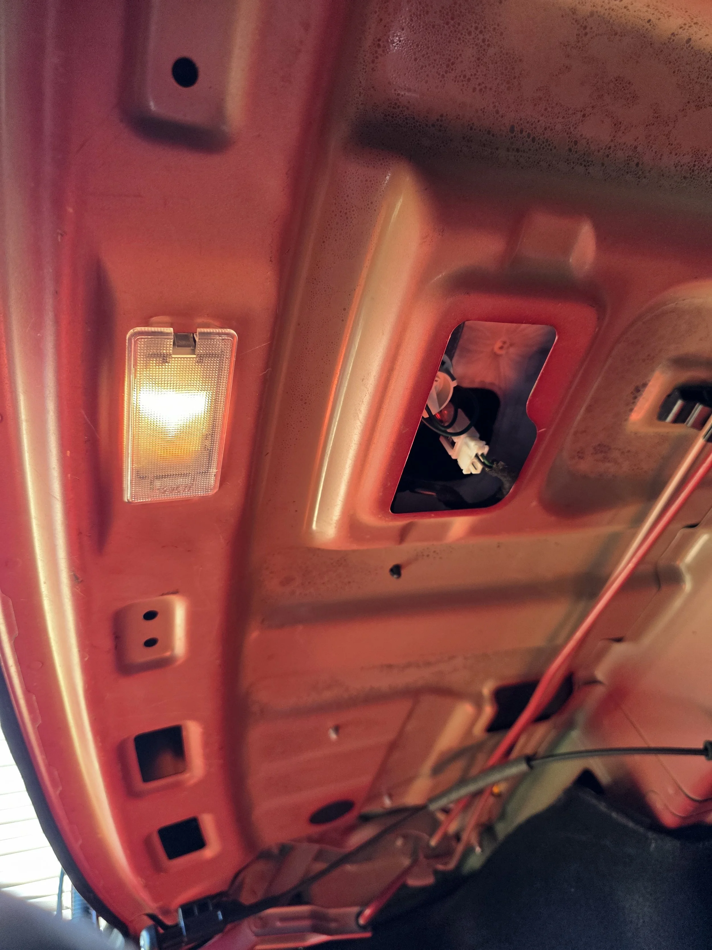 The underside of a vehicle's hood with the interior components and wiring visible, including a lit overhead light.